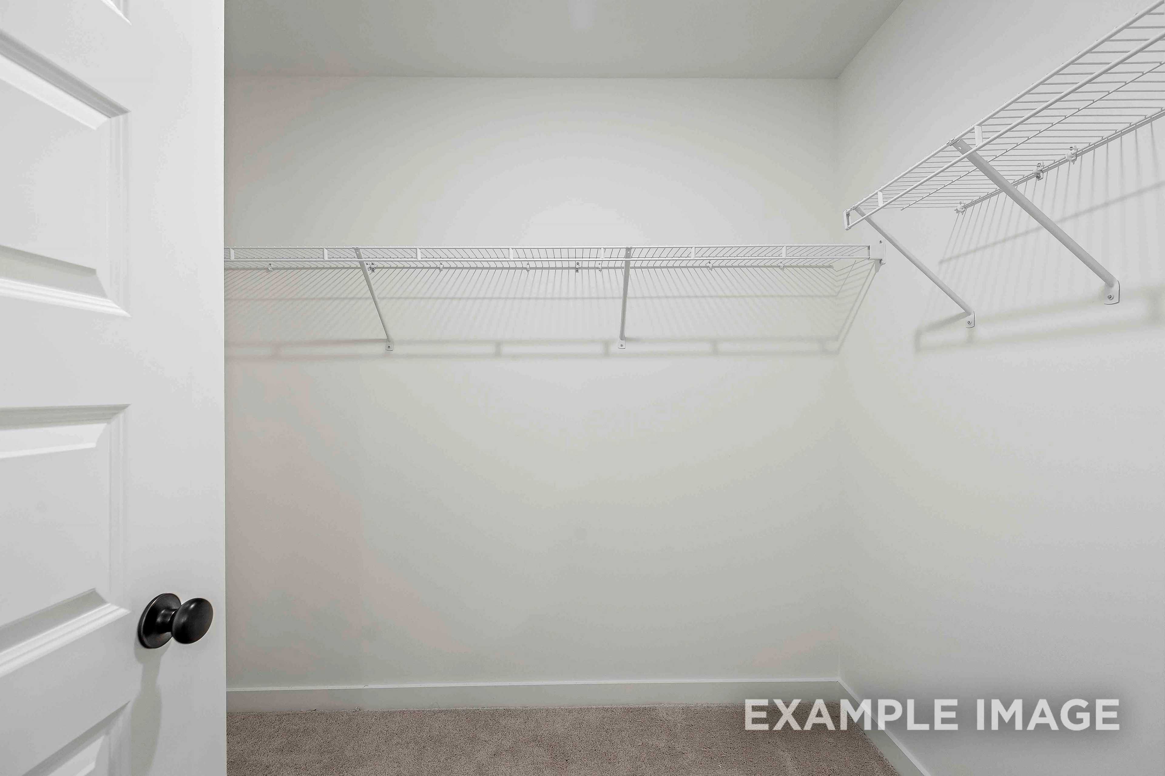 Spacious walk-in closet in The Charleston master suite with wire shelving, hanging rods, and beige carpet flooring