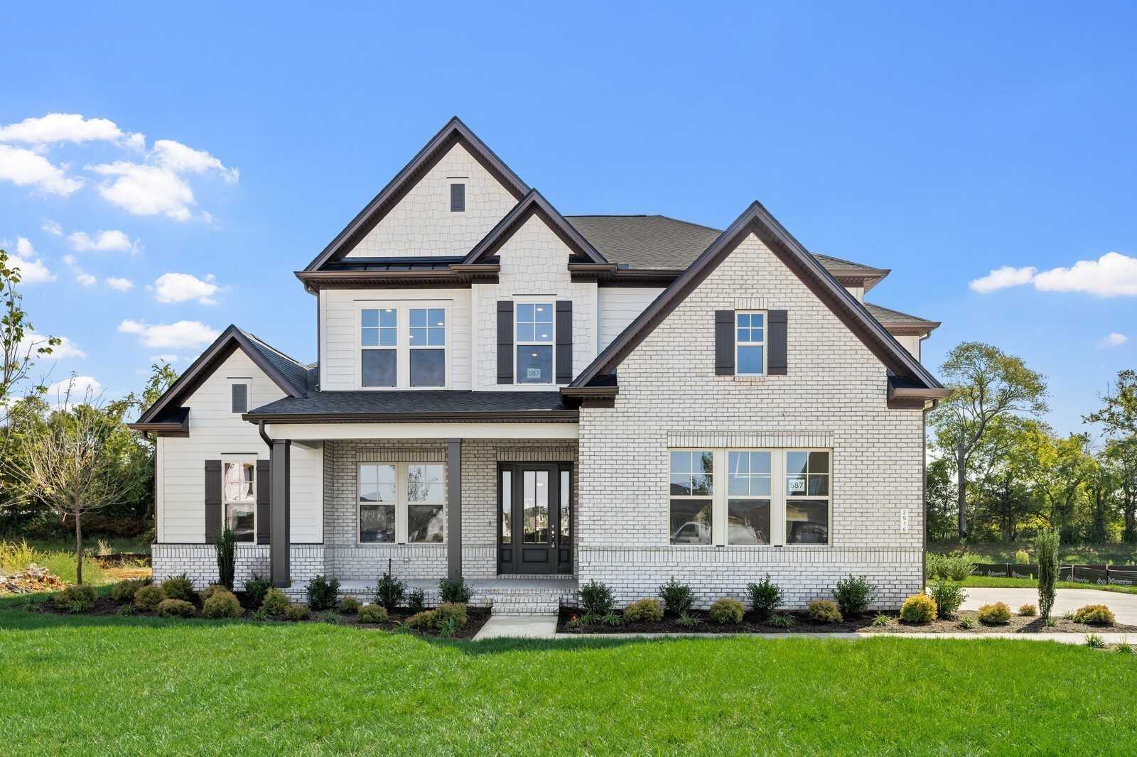 Two-story white brick home with black shutters, covered porch, and lush landscaping in Shelton Square, Murfreesboro, TN by Davidson Homes The Albany A