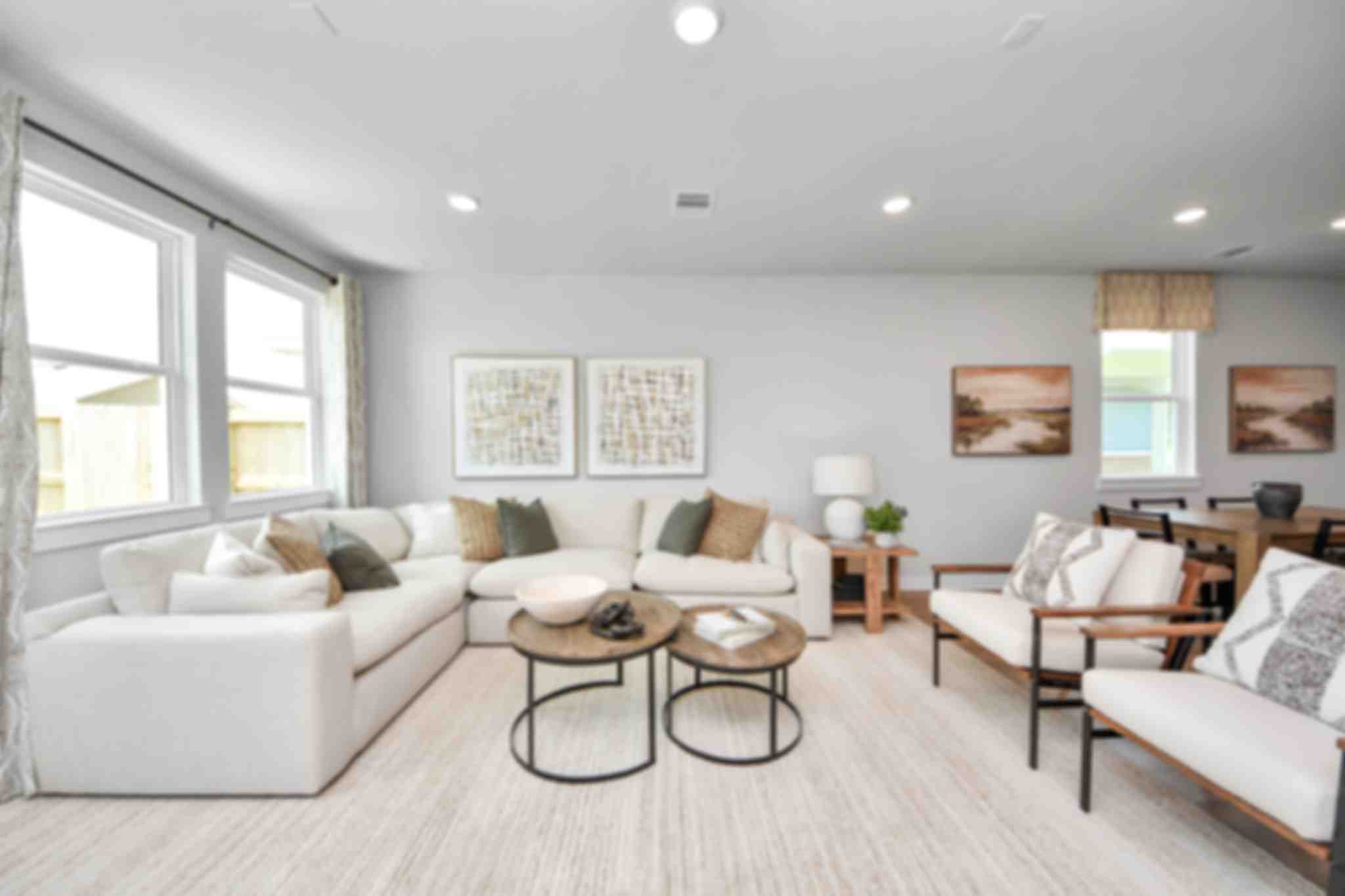 Spacious modern living room at Robins Landing in Houston TX with hardwood floors, green velvet armchairs, beige sectional sofa, and large windows