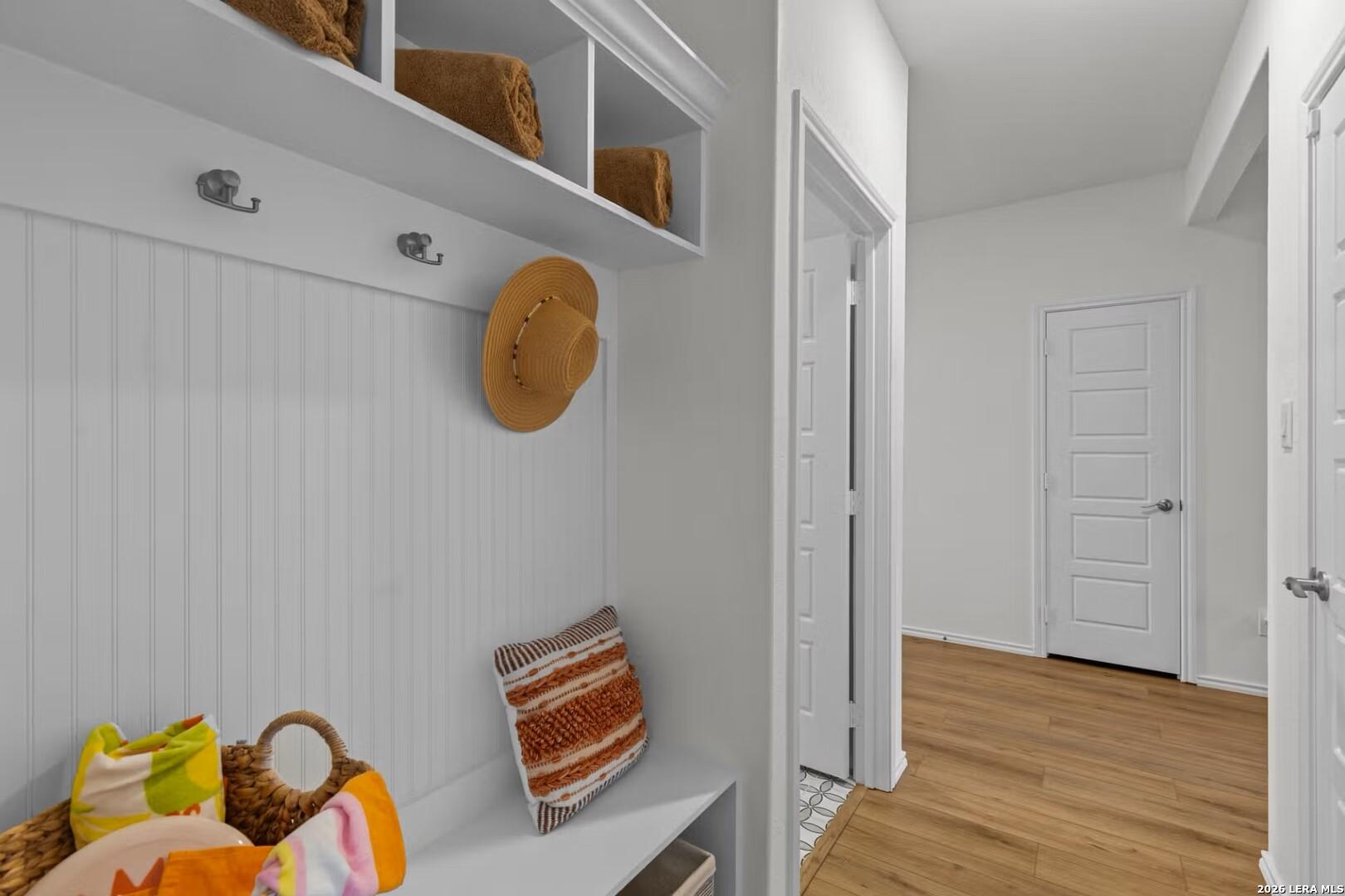 Organized mudroom with white beadboard walls, towel shelves, straw hat hooks, and bench with woven pillow in Davidson Homes The Daphne K, Bricewood San Antonio