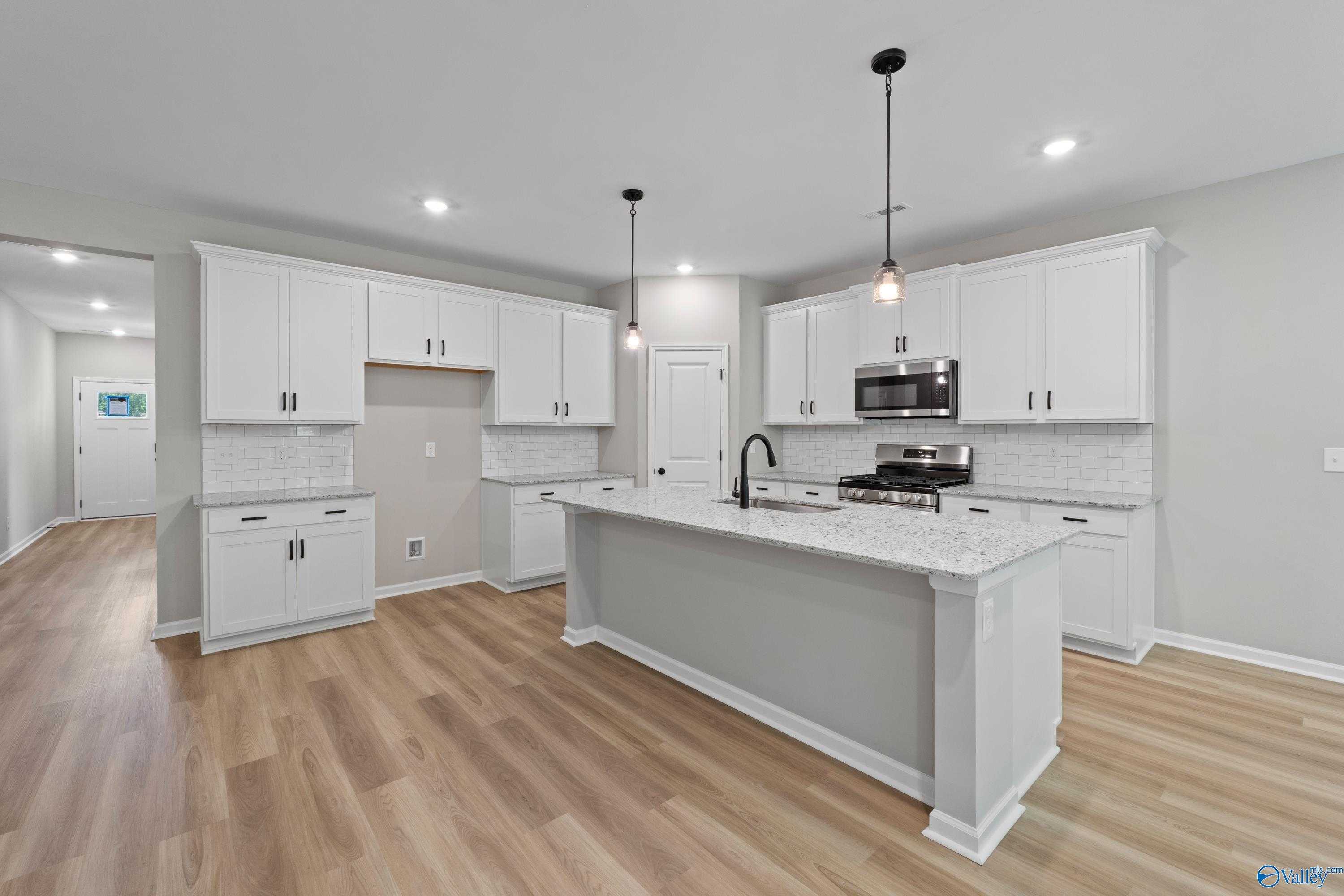 Modern white kitchen with quartz island, stainless appliances, pendant lights in Davidson Homes The Phoenix, Hazel Green, AL