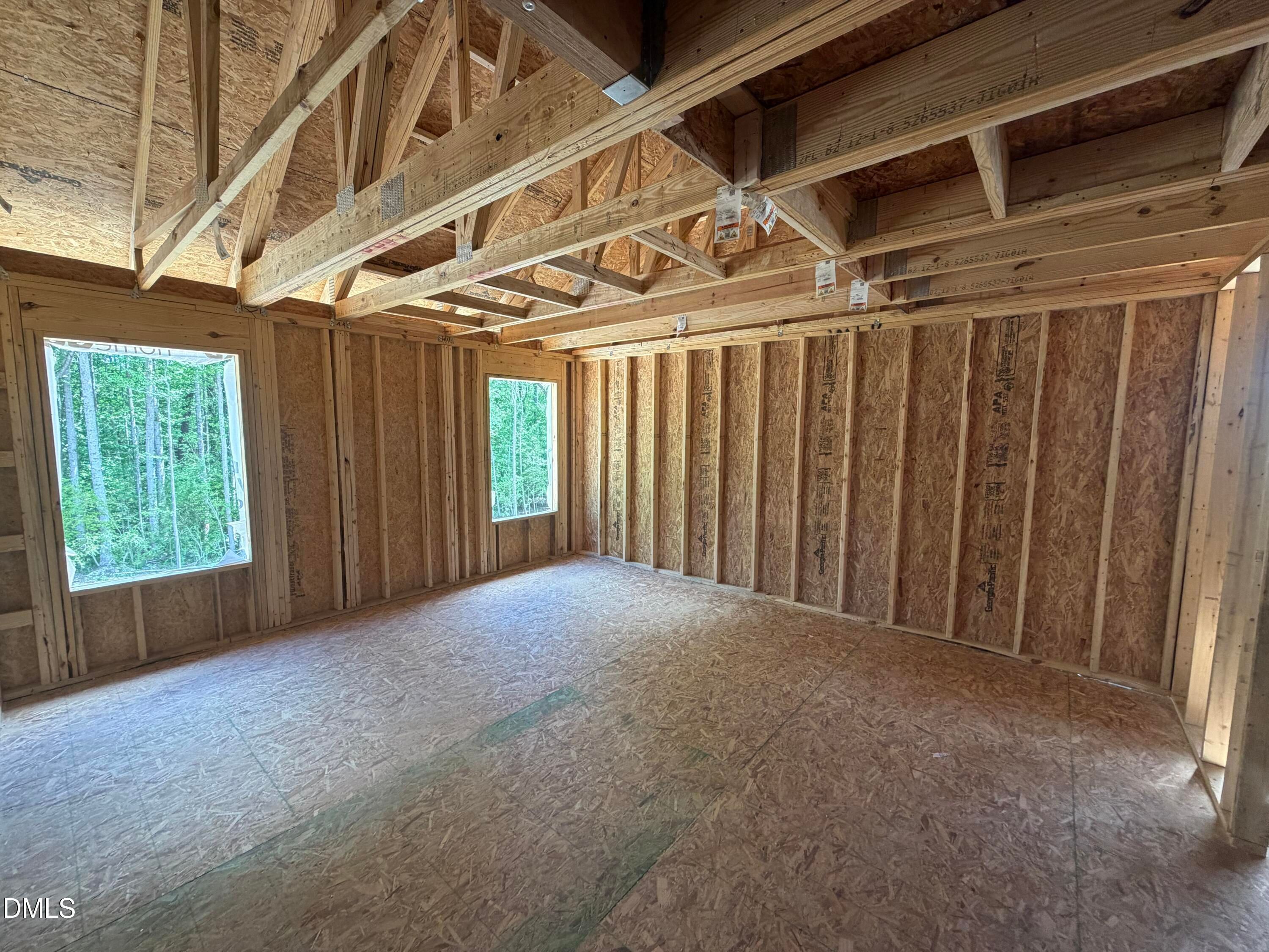 Exposed wooden trusses, OSB walls, and plywood subfloor in spacious unfinished room with large windows overlooking woods, The Hickory II C by Davidson Homes, Lillington NC
