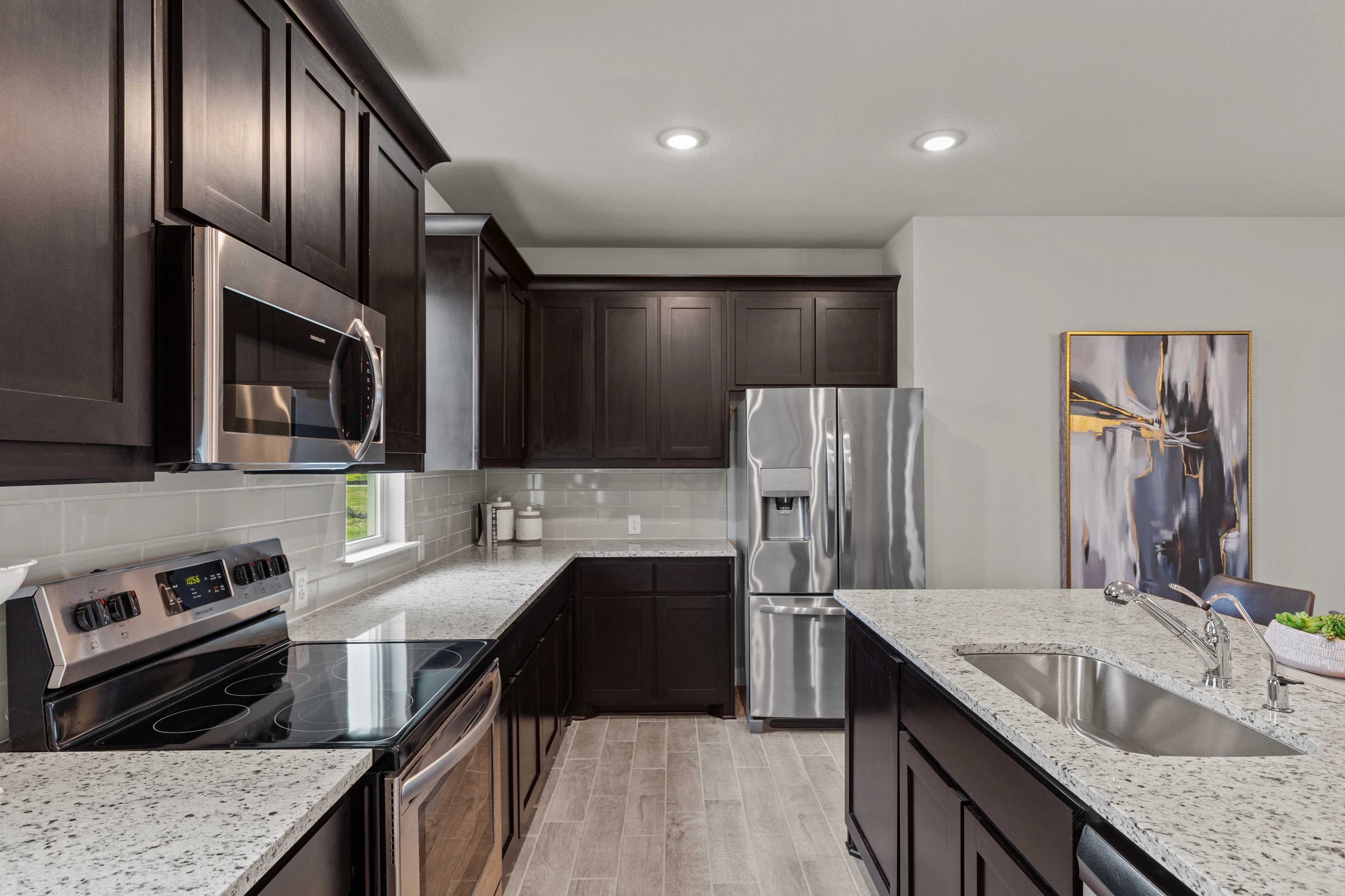 Spacious modern kitchen in Hannah Heights Seguin Texas with dark wood cabinets, stainless steel appliances, quartz island and light wood floors