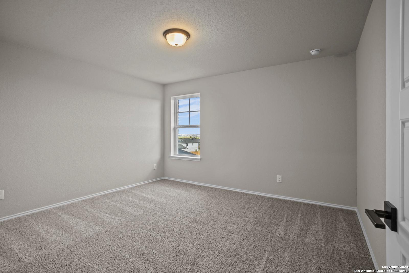 Bright empty bedroom with neutral walls, carpet flooring, and large window in Davidson Homes The Douglas F, San Antonio, Texas