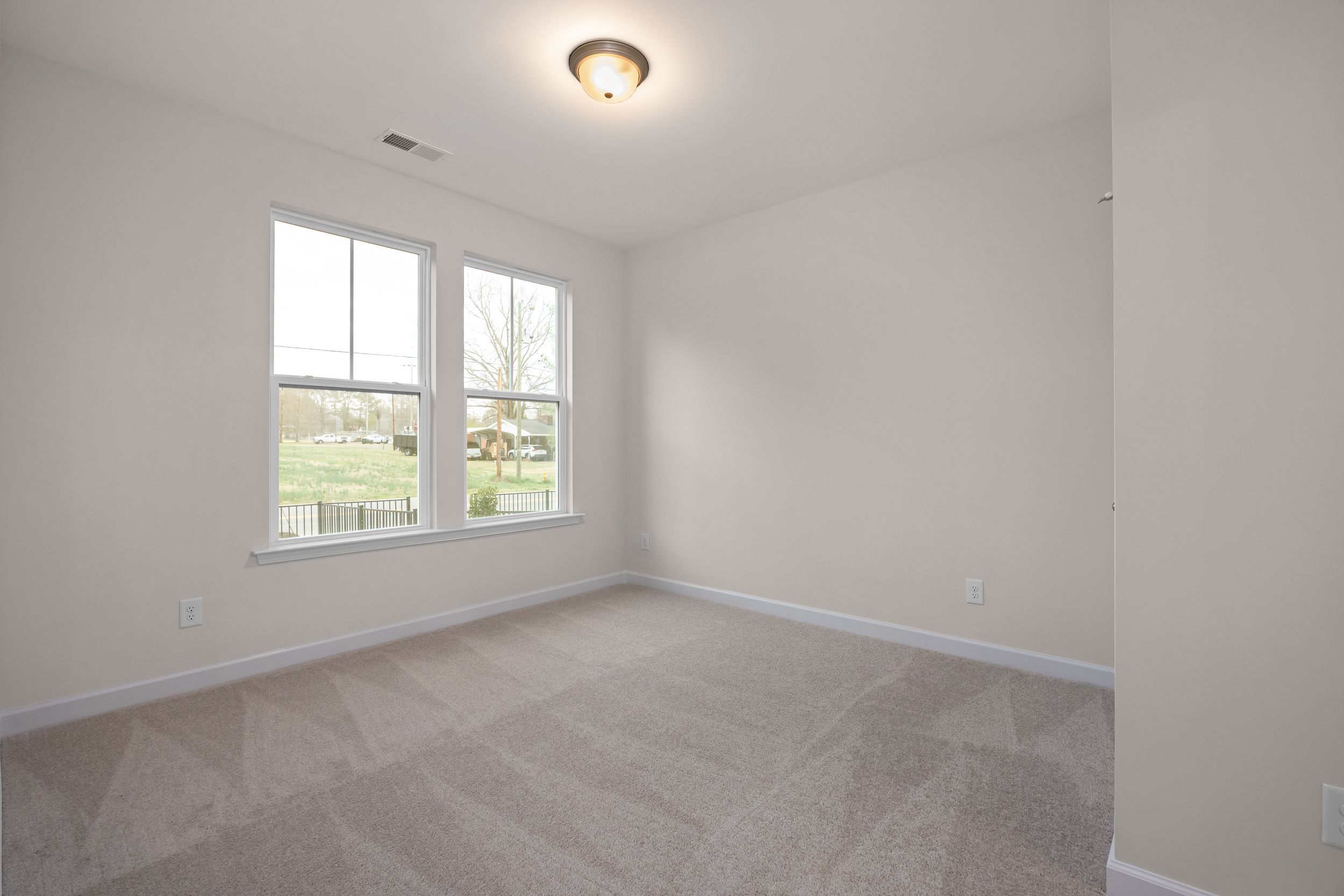 Spacious bedroom with large windows overlooking wooded yard, gray carpet, white walls at Forestville Yard Townhomes Knightdale NC