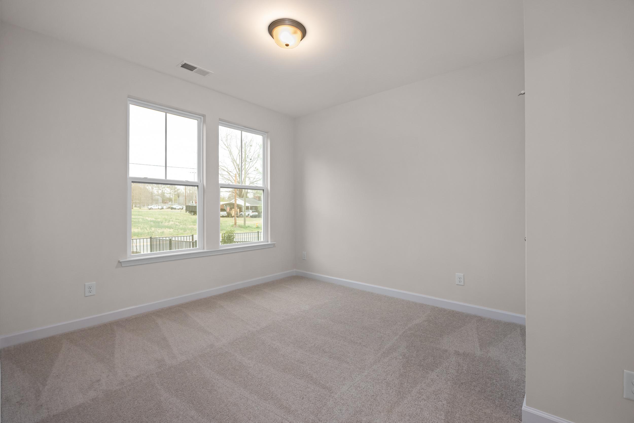 Spacious bedroom with large windows overlooking wooded yard, gray carpet, white walls at Forestville Yard Townhomes Knightdale NC