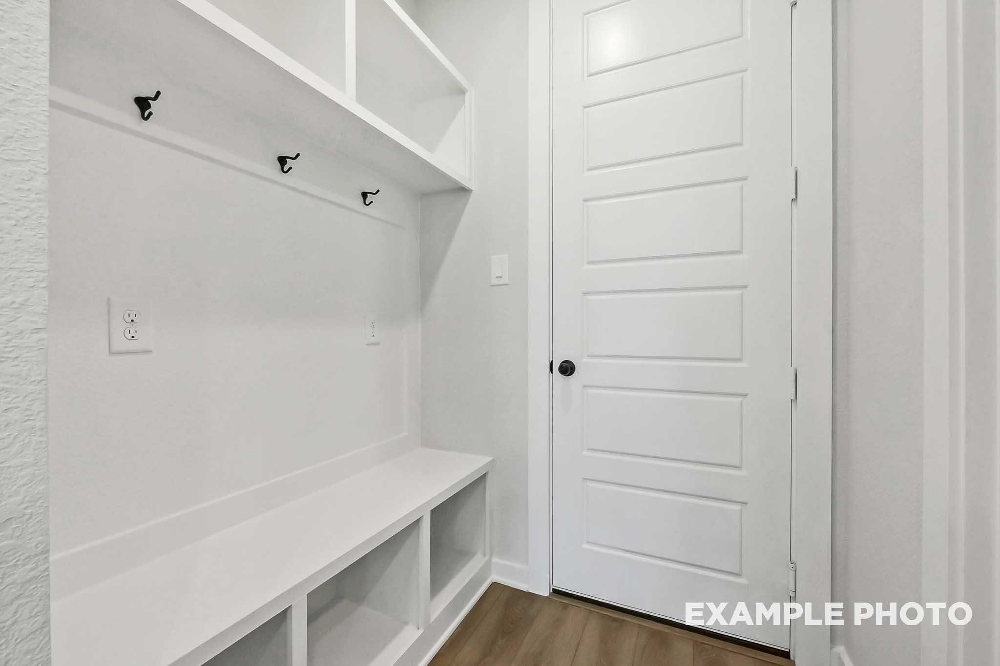 Modern mudroom in The Sequoia home with white built-in bench, coat hooks, and open shelving by Davidson Homes