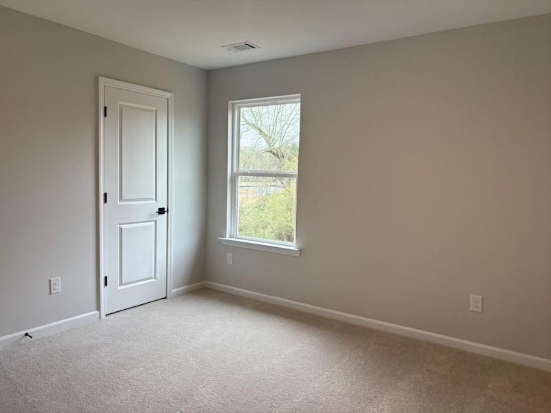Empty bedroom with light gray walls, white double door, large window overlooking trees, and beige carpet in Davidson Homes The Hickory B, Winder, GA