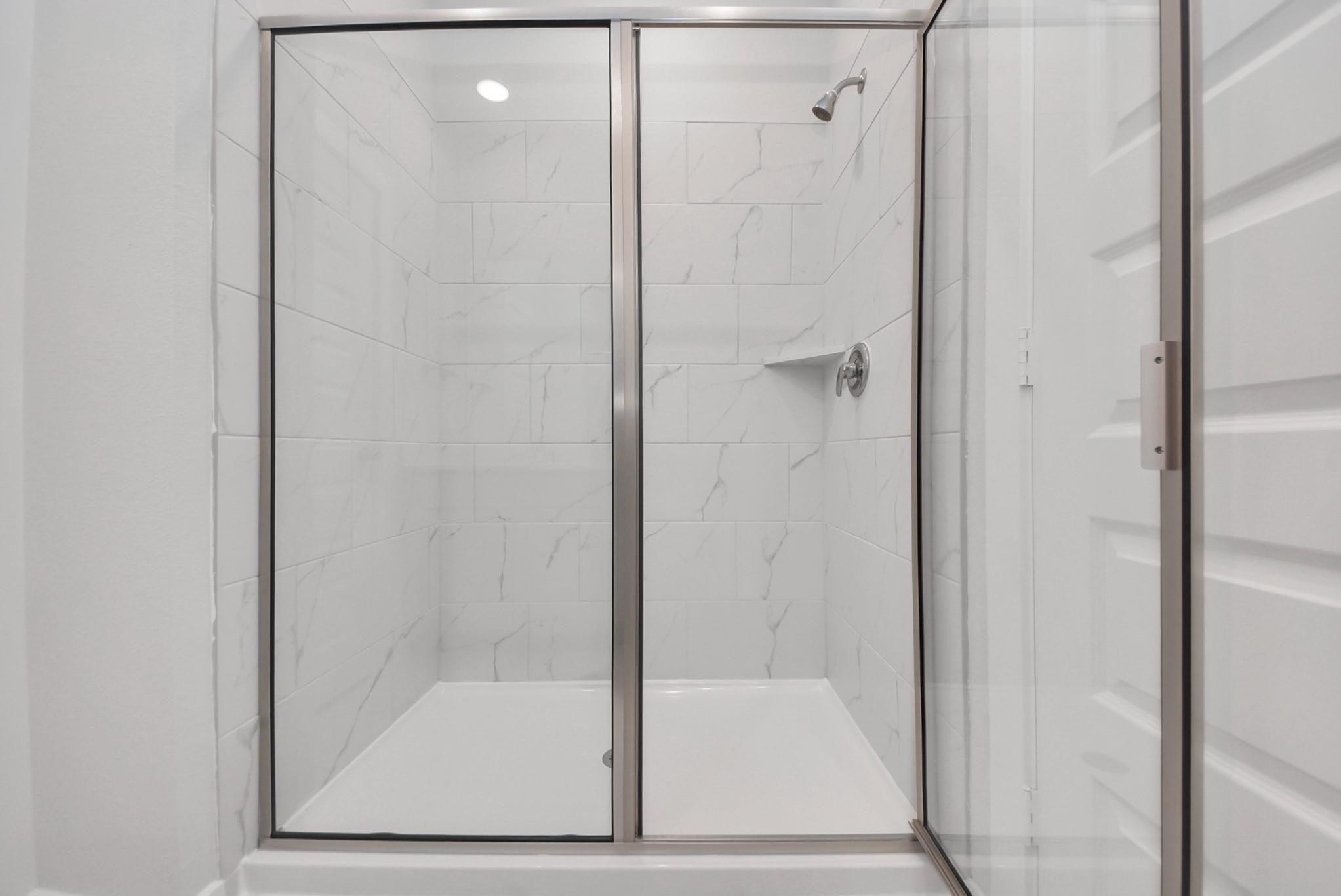 Elegant glass-enclosed shower with marble-look tile in modern bathroom of Davidson Homes The San Marcos E, Beasley, Texas