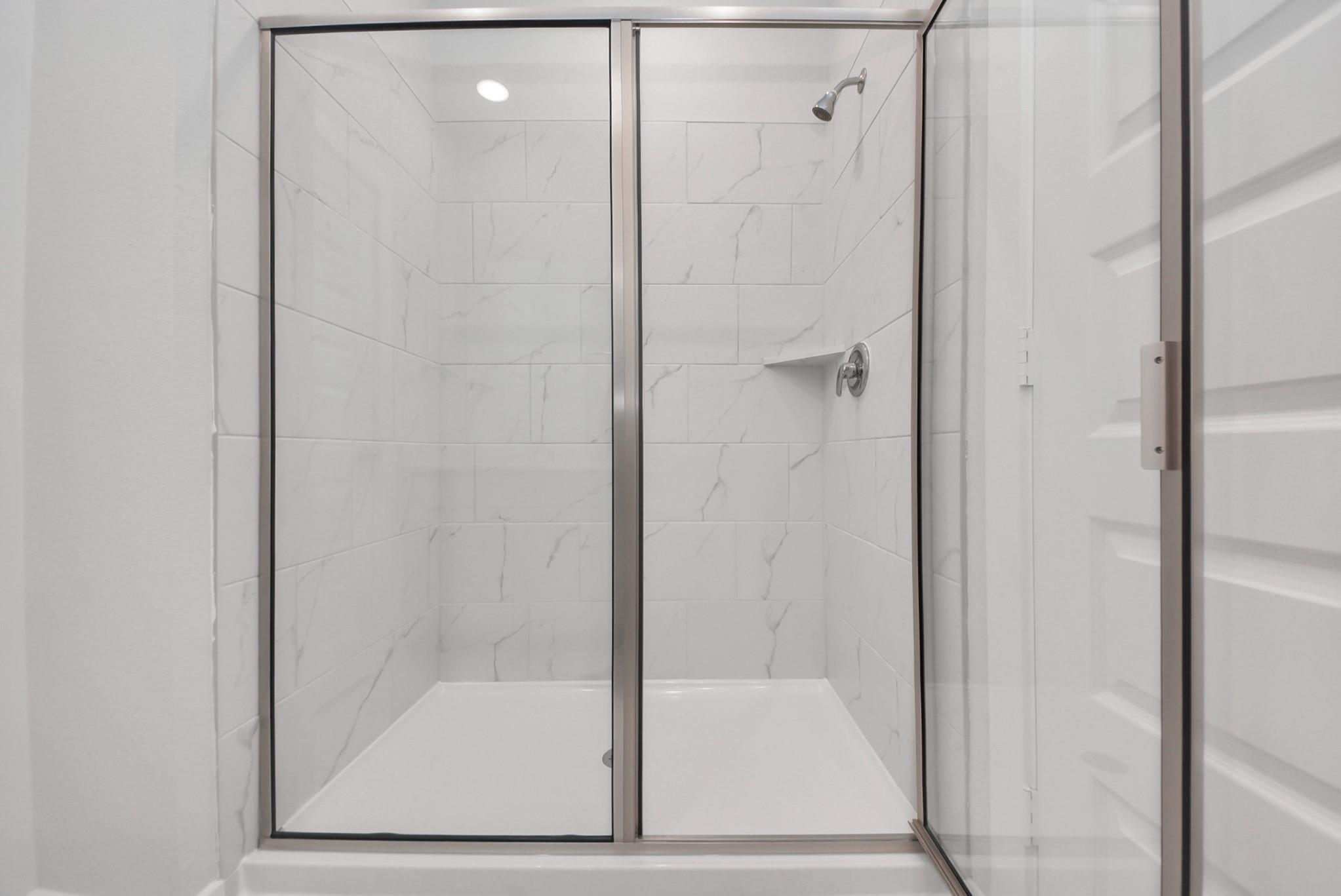 Elegant glass-enclosed shower with marble-look tile in modern bathroom of Davidson Homes The San Marcos E, Beasley, Texas