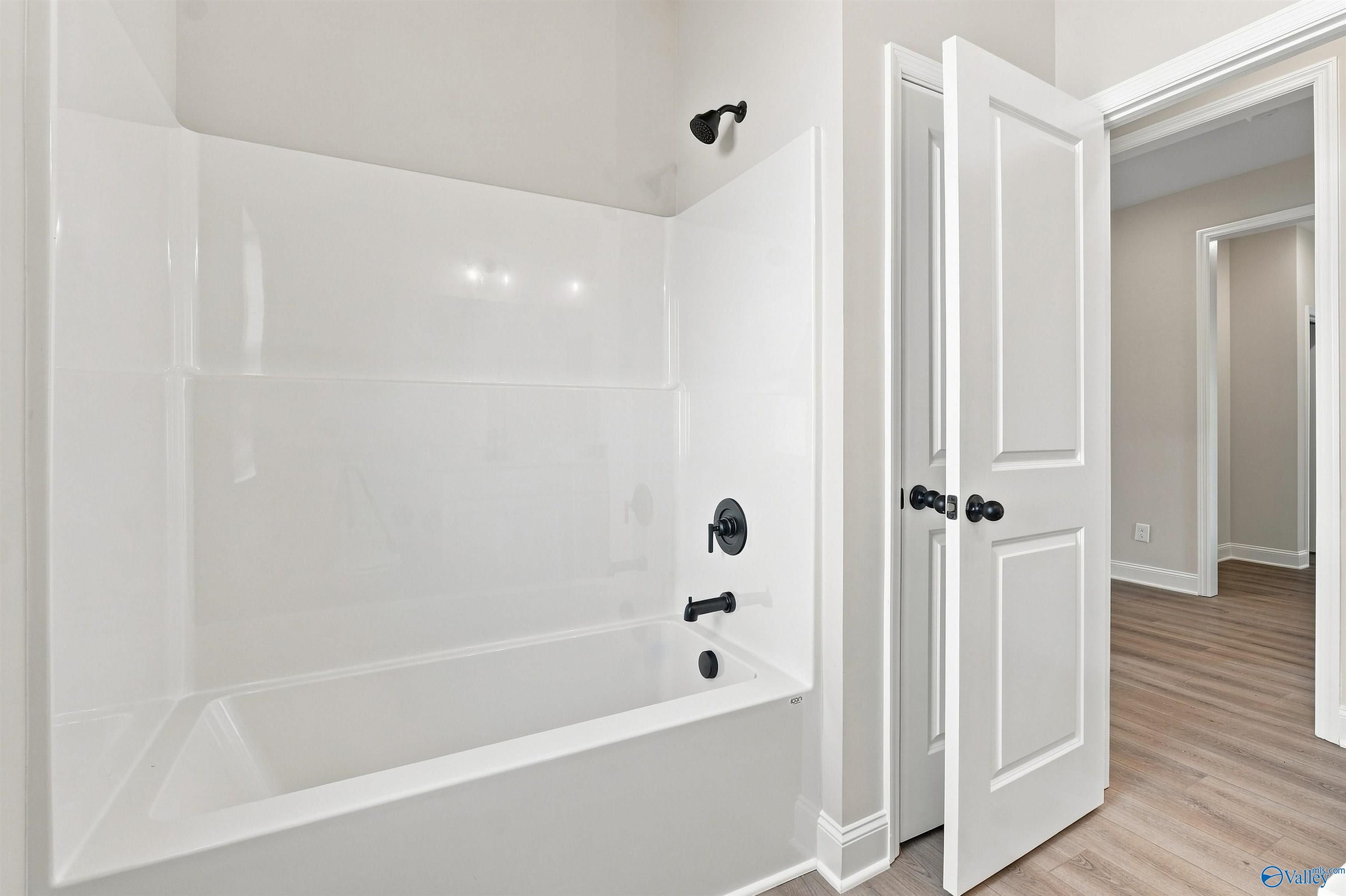 White tub shower combo with matte black fixtures beside white double doors in Davidson Homes Everett B bathroom, Toney, Alabama