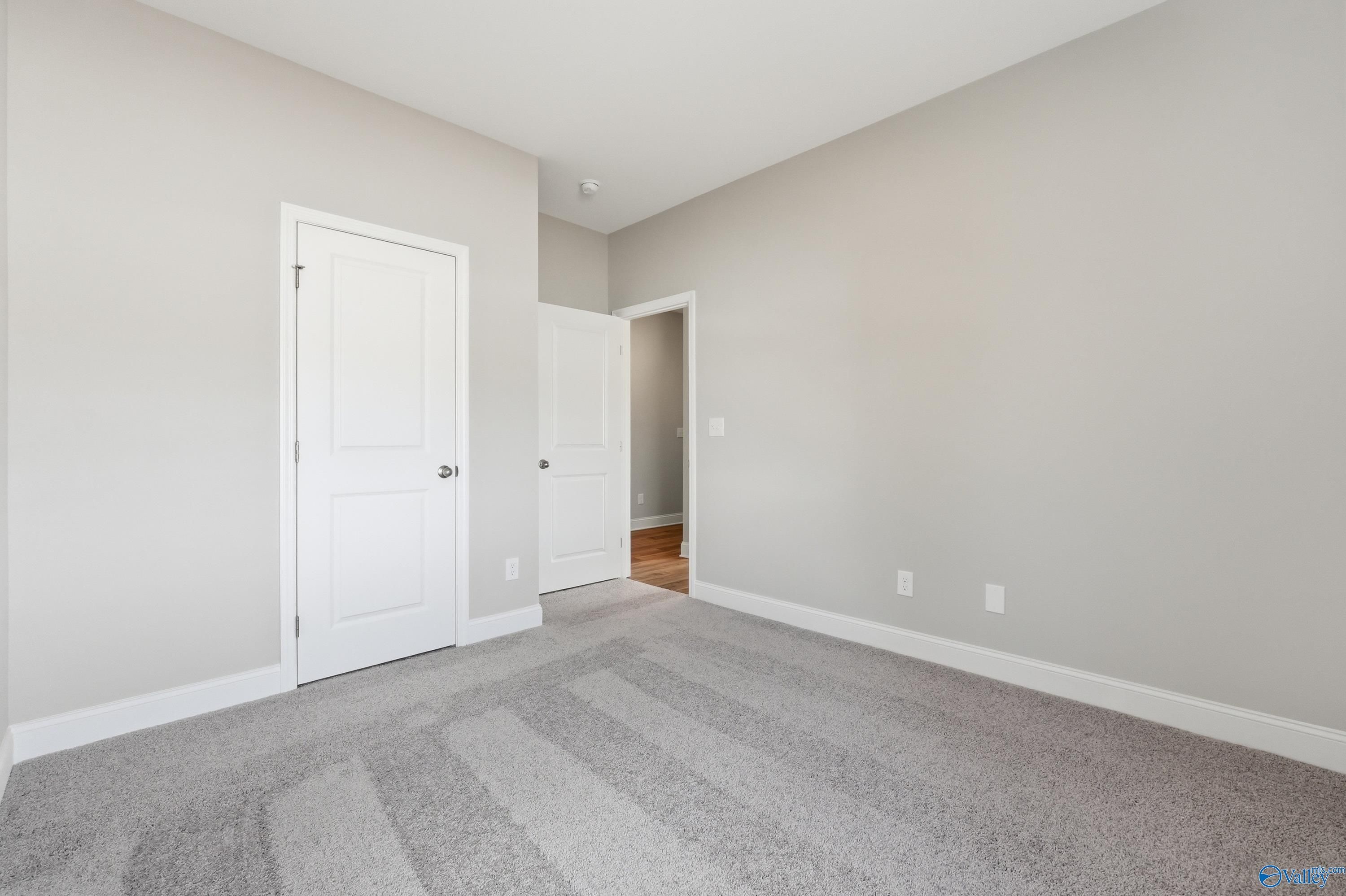 Spacious empty bedroom with light gray walls, white paneled doors, and gray carpet in Davidson Homes The Asheville, Huntsville AL