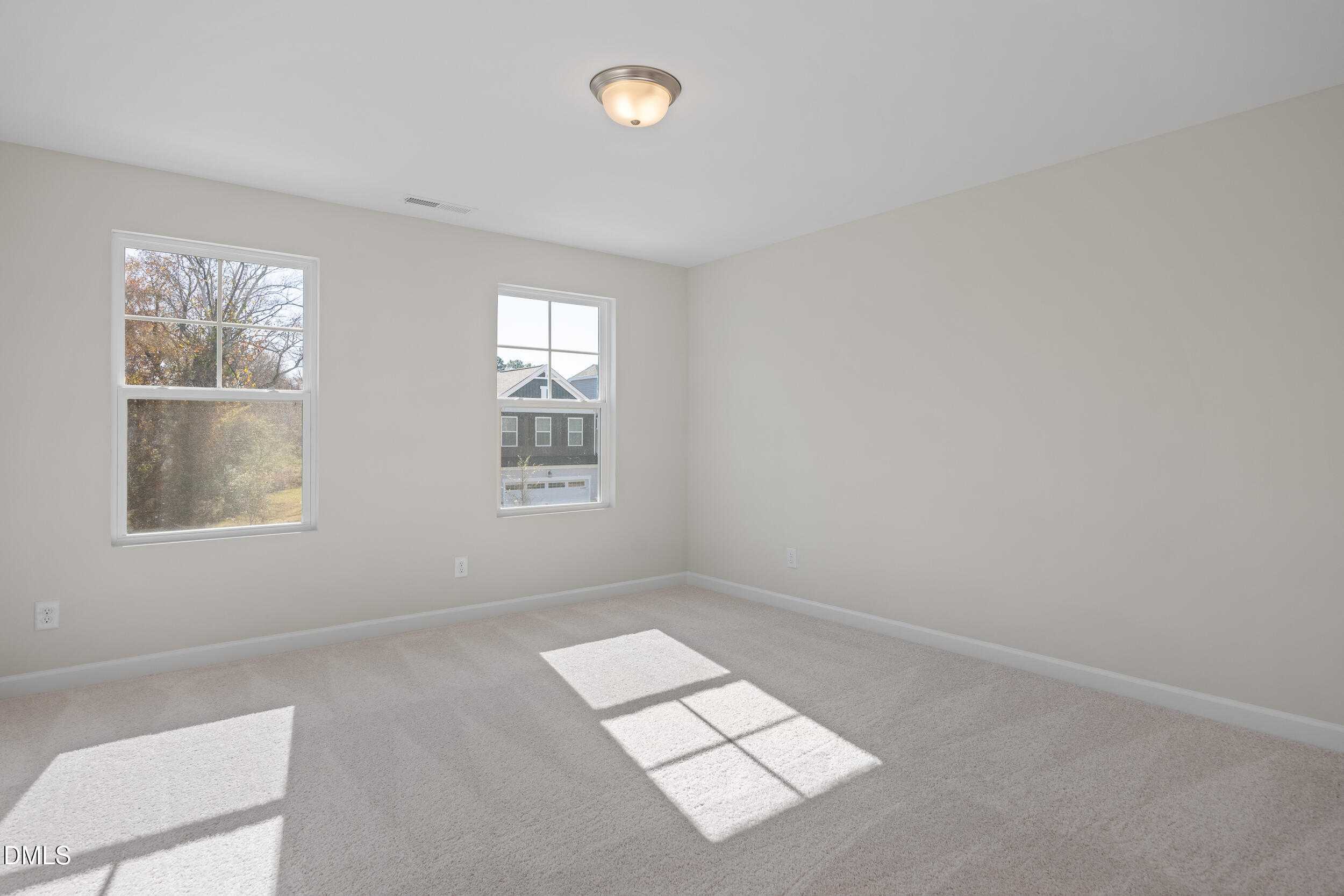 Bright empty bedroom with beige walls, carpet floor, large windows, and natural sunlight in Davidson Homes Preston C, Lillington, NC