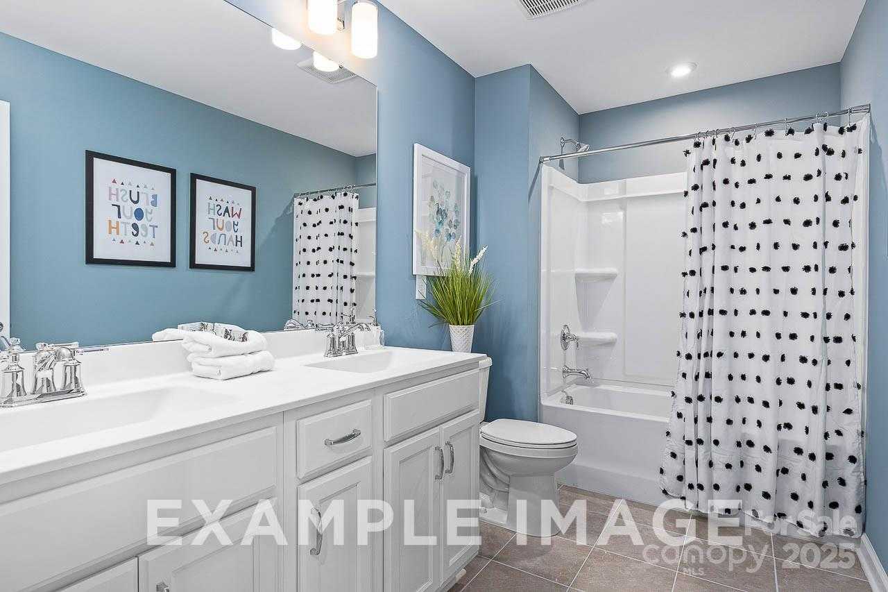 Modern blue bathroom with double vanity, polka dot shower curtain, and artwork in Davidson Homes The Hemlock A, Enclave at Belmont