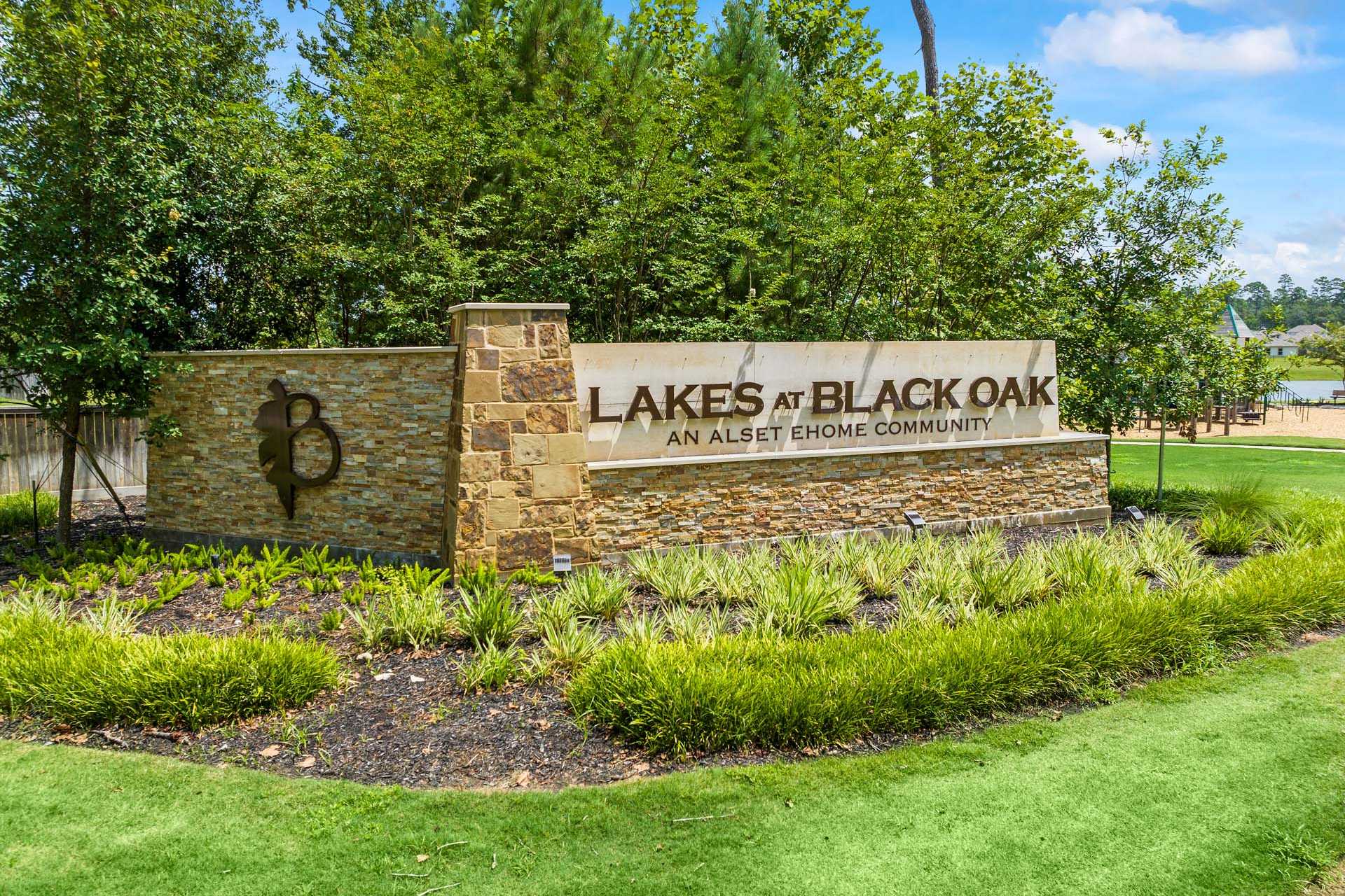 Entrance sign at Lakes at Black Oak, an Ashton Homes community in Magnolia Texas with stone pillars, lush greenery and pond view