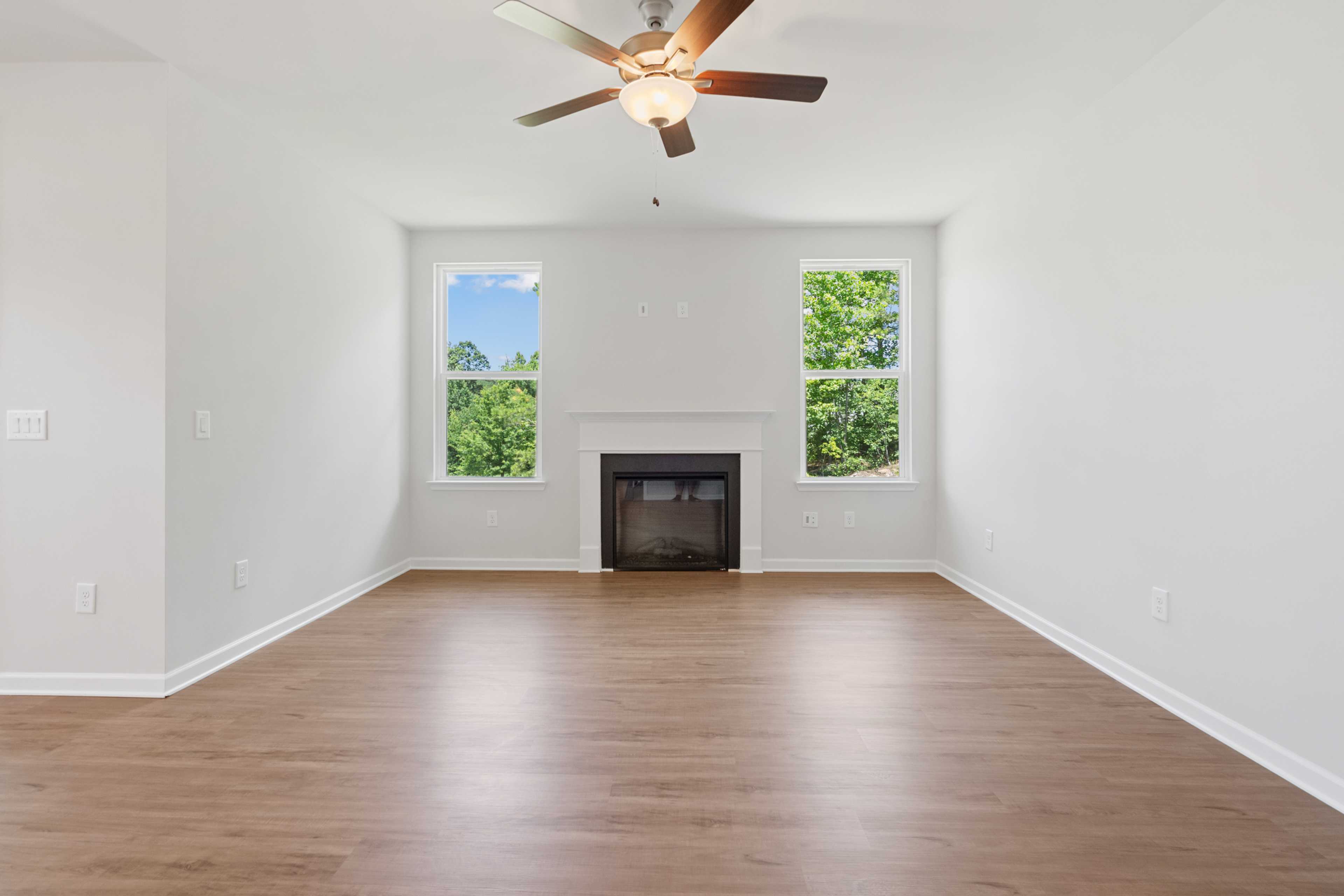 Spacious empty living room in Mountainbrook Cartersville GA with hardwood floors, gas fireplace, ceiling fan, and large windows