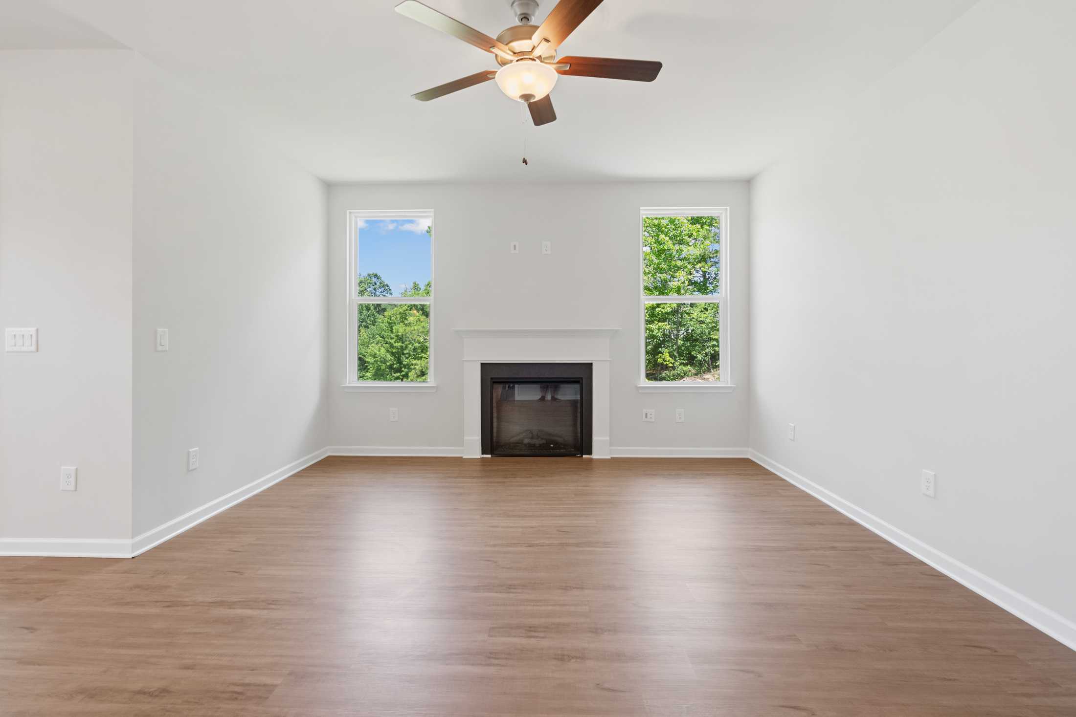 Spacious empty living room in Mountainbrook Cartersville GA with hardwood floors, gas fireplace, ceiling fan, and large windows