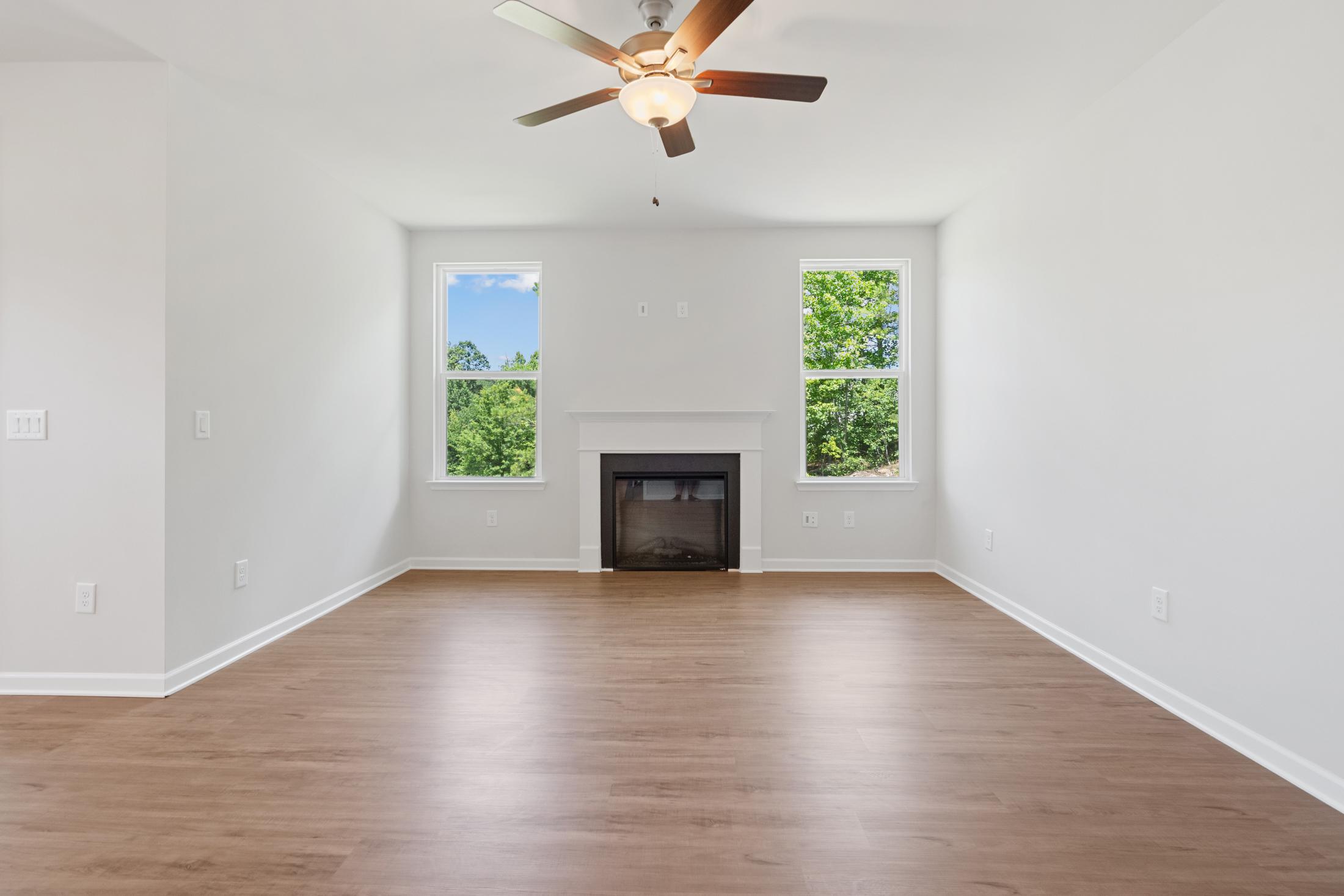 Spacious empty living room in Mountainbrook Cartersville GA with hardwood floors, gas fireplace, ceiling fan, and large windows