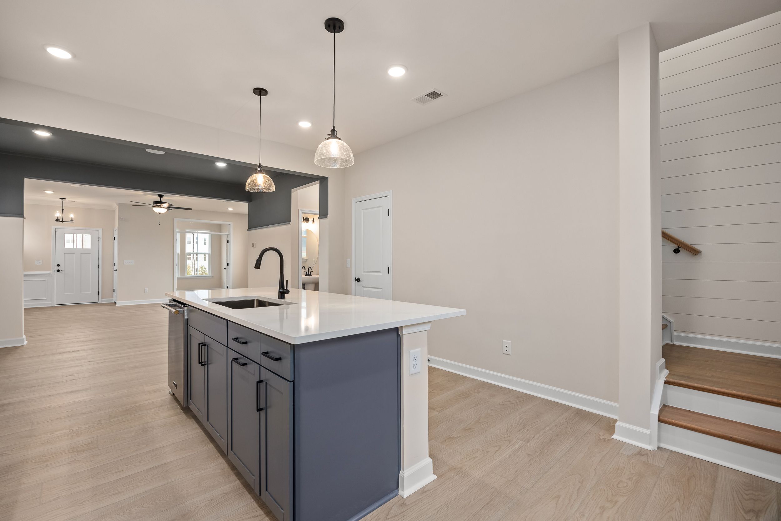 Open-concept kitchen at Forestville Yard in Knightdale NC featuring navy island, white quartz counters, pendant lights, hardwood floors, and stairs