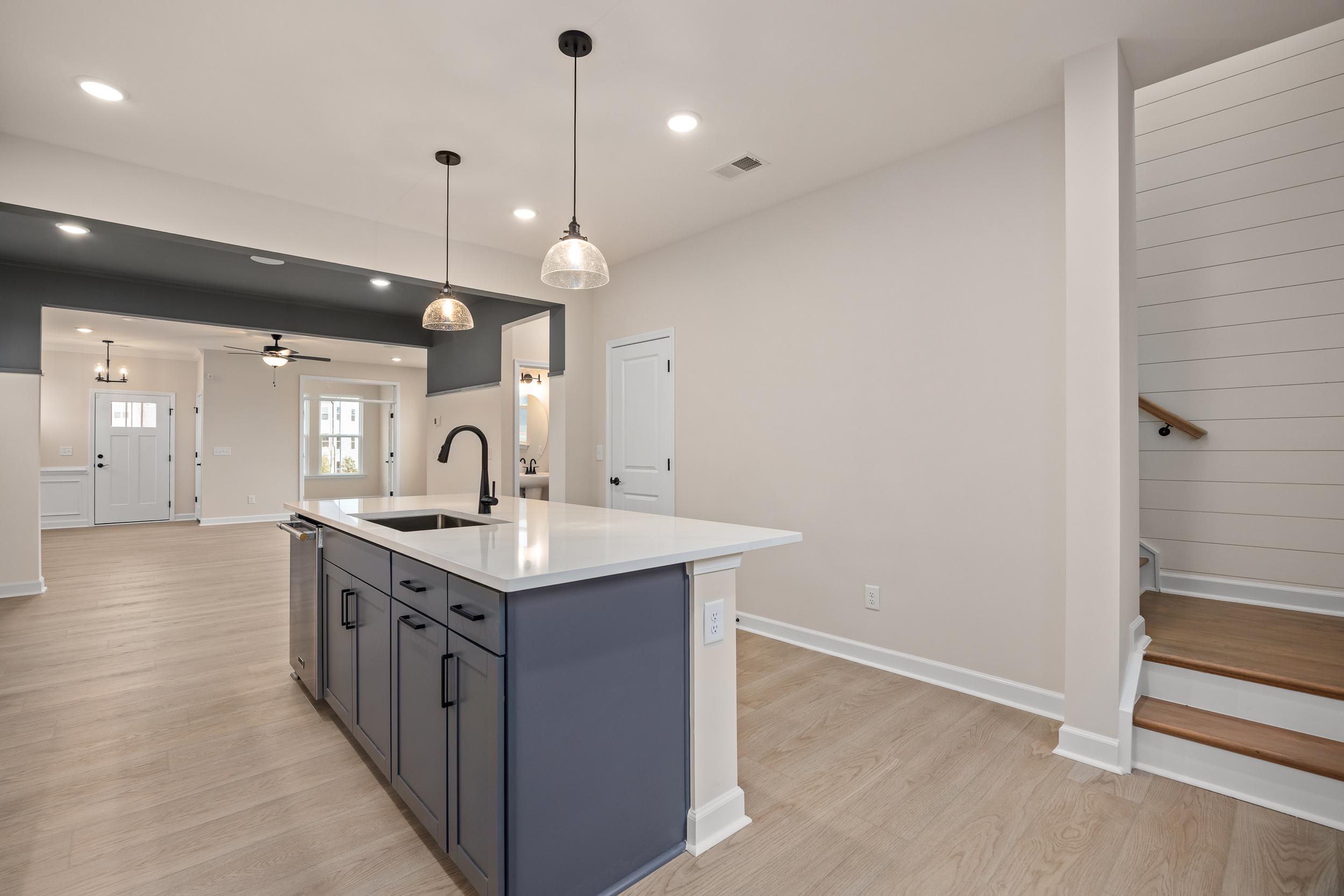 Open-concept kitchen at Forestville Yard in Knightdale NC featuring navy island, white quartz counters, pendant lights, hardwood floors, and stairs