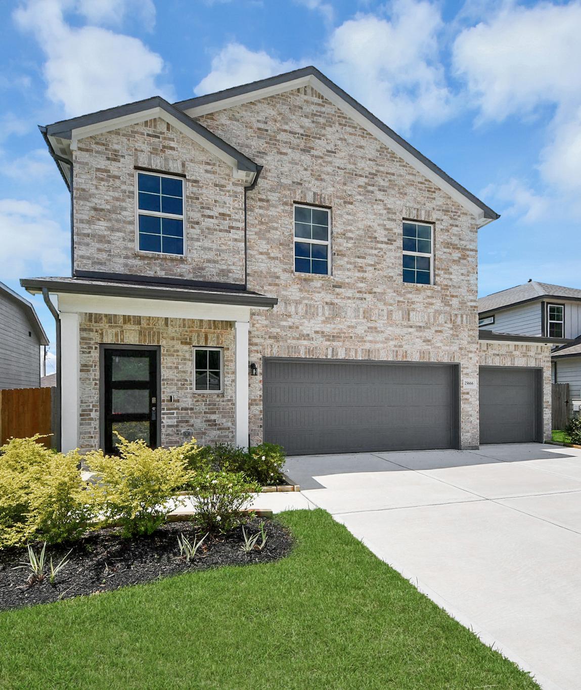Brick home exterior at Hill & Dale Ranch in Splendora TX with covered porch, flagpoles, flower beds, and stone walkway
