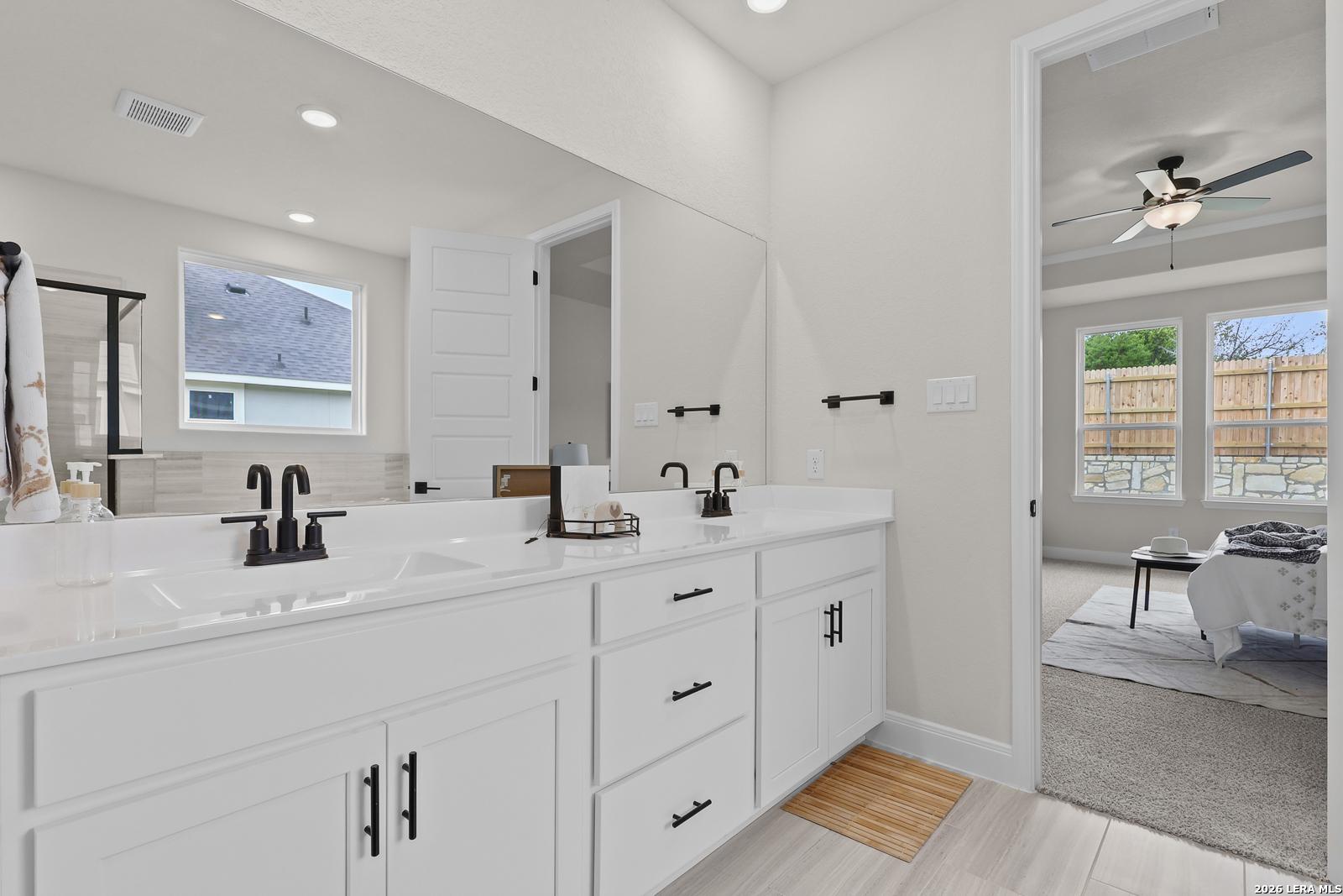 Modern master bathroom featuring double white vanity, quartz countertop, bronze faucets, and large mirror in Davidson Homes The Lanier G, Castroville, Texas