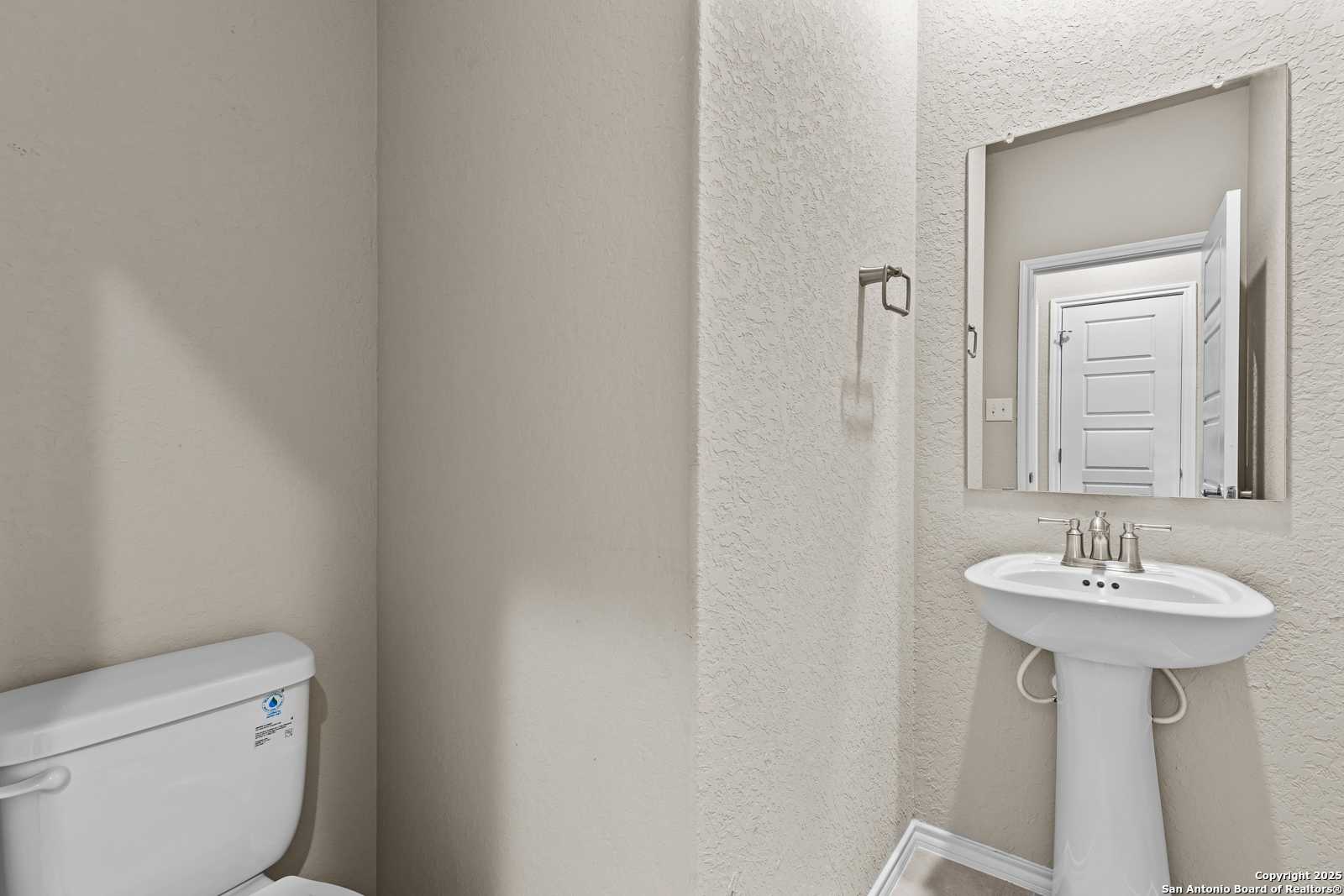 Elegant powder room with pedestal sink, mirror, and open door in The Douglas F by Davidson Homes, San Antonio