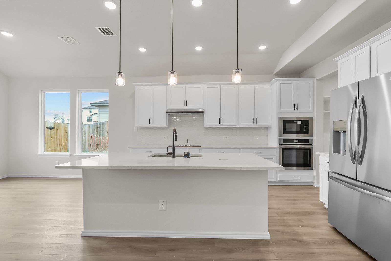 Modern white kitchen in The Sequoia C featuring a large center island, stainless appliances, and pendant lighting.
