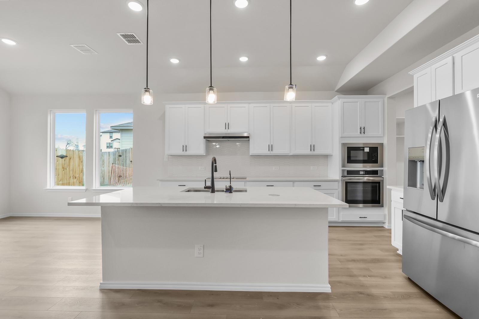 Modern white kitchen in The Sequoia C featuring a large center island, stainless appliances, and pendant lighting.