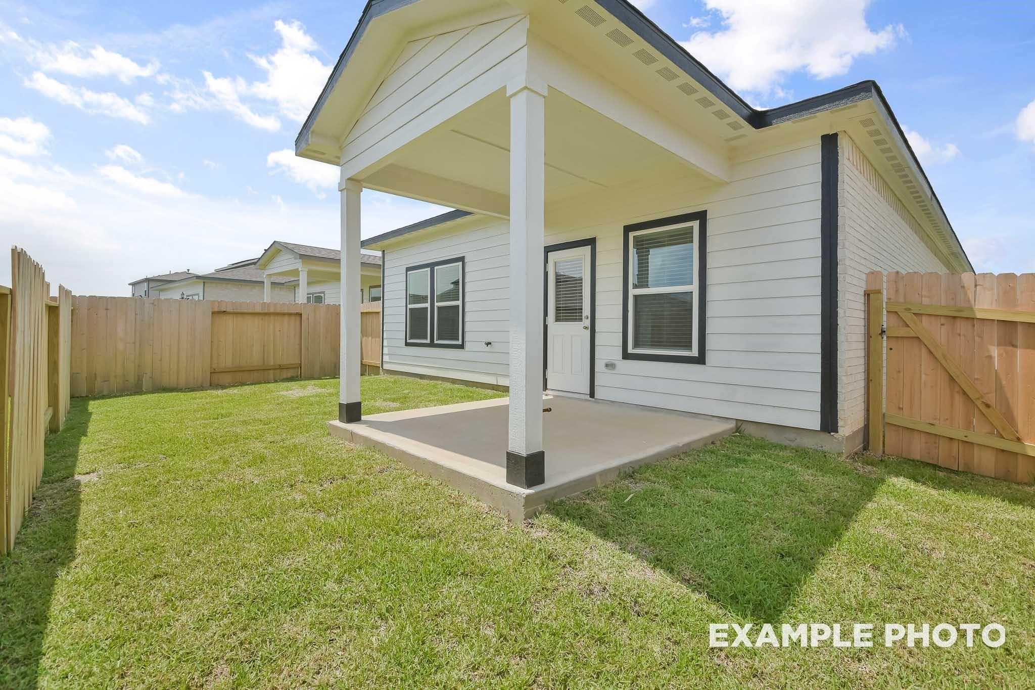 Covered back patio with white posts, wooden fence, and lush green yard in Davidson Homes The Frio F, Conroe, Texas