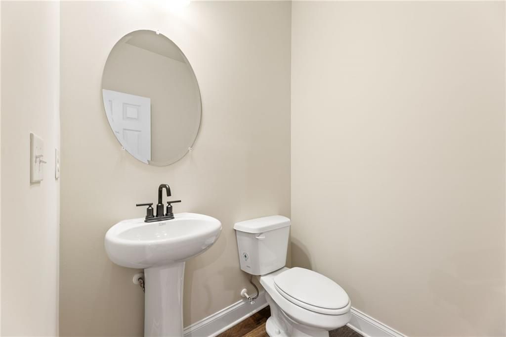 Elegant powder room featuring white pedestal sink, round mirror, and toilet in Davidson Homes The Harrison H, Winder, Georgia