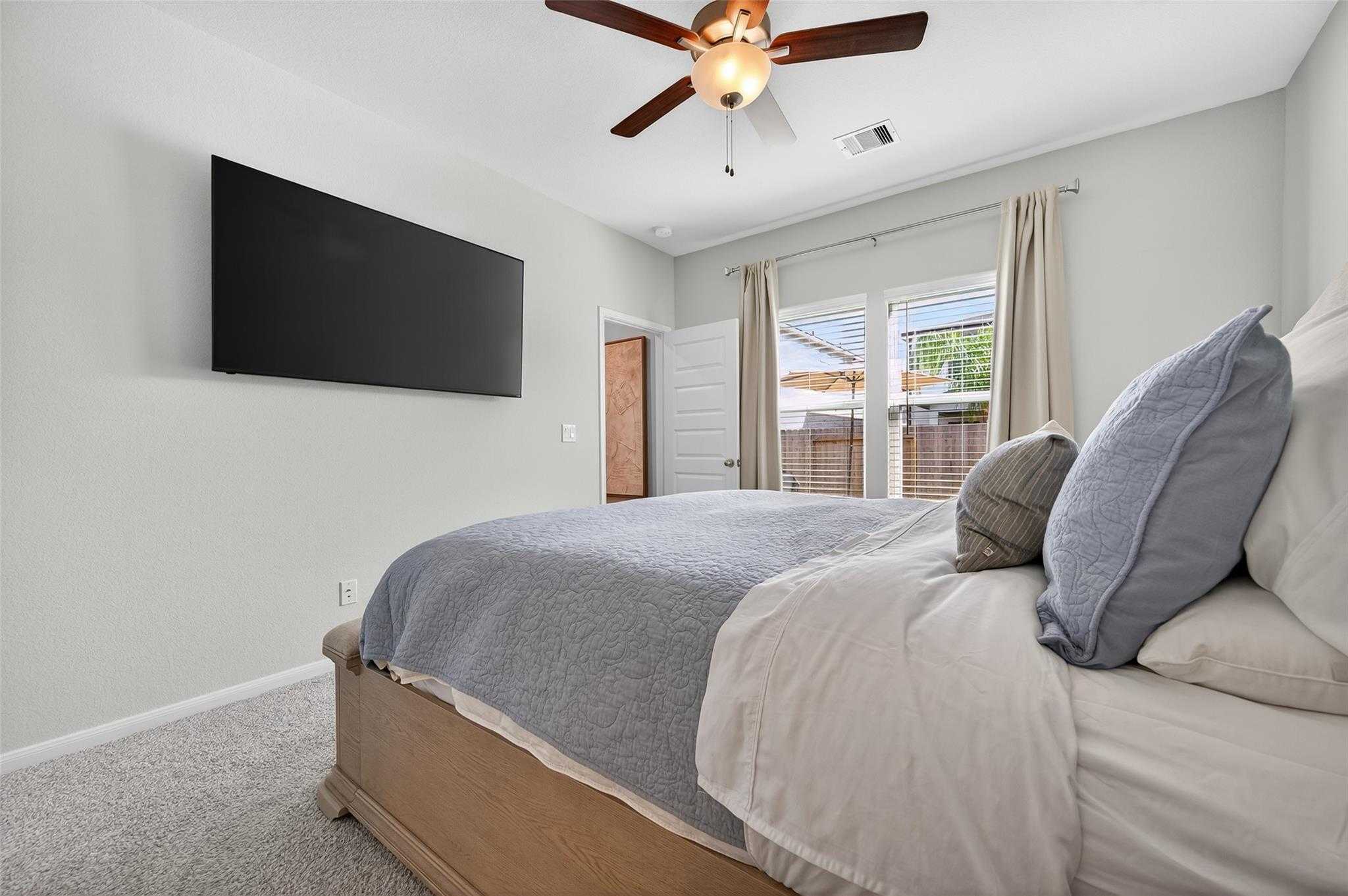 Cozy secondary bedroom with ceiling fan, wall-mounted TV, plush gray bedding, and sliding doors to backyard in Davidson Homes The Brazos E, Magnolia, Texas