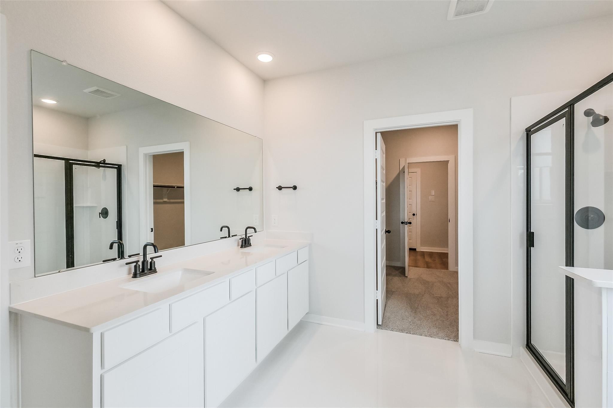 Modern master bathroom with dual white vanity sinks, quartz counters, and frameless glass shower in Davidson Homes Tierra B, Beasley, Texas