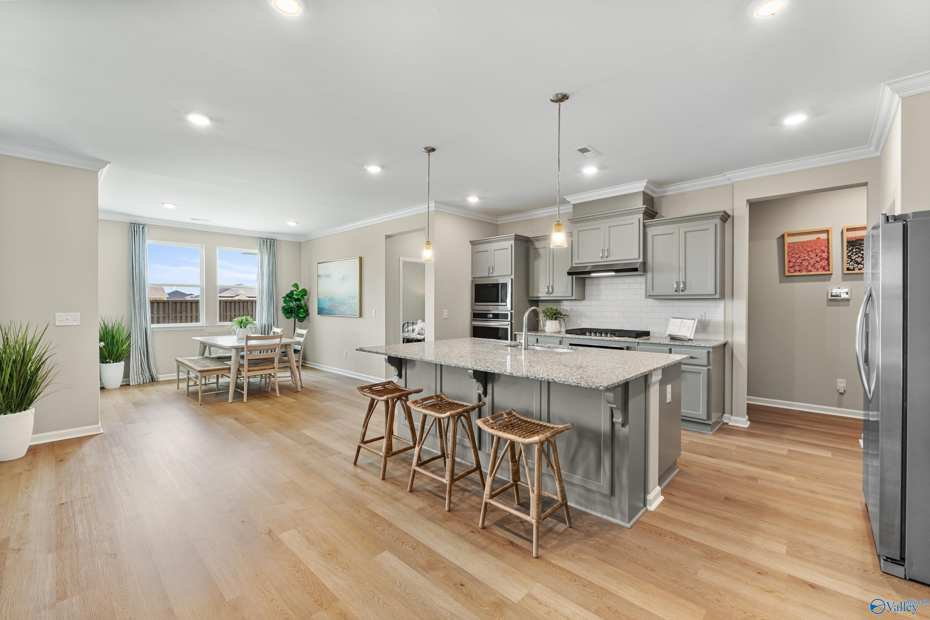 Open-concept kitchen with gray island, wood stools, stainless appliances, and dining nook in Davidson Homes The Sanctuary, Athens AL