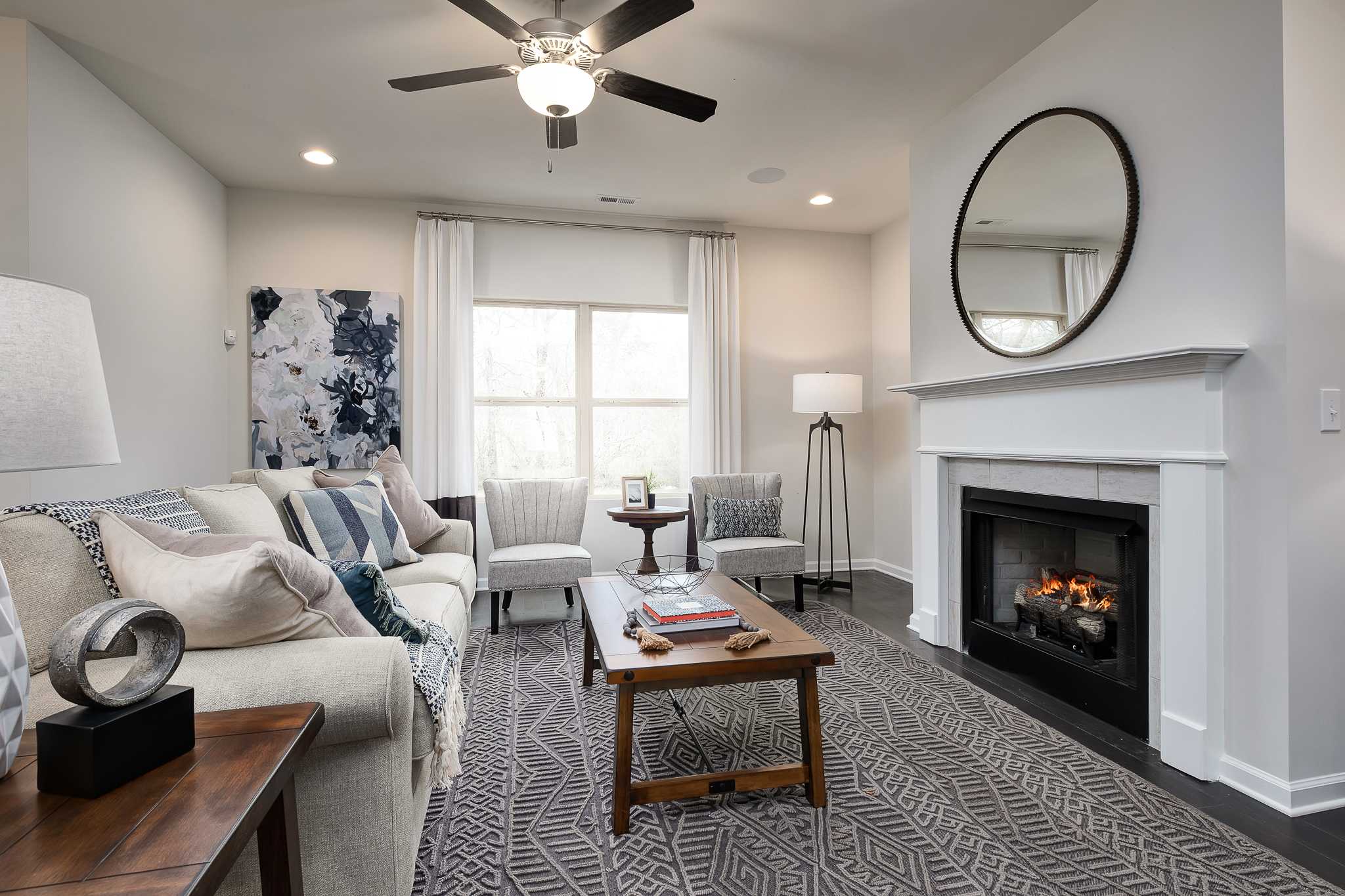 Cozy living room with white fireplace, plush sofa, patterned rug, and ceiling fan at The Reserve at Overton in Hampton Cove, Alabama