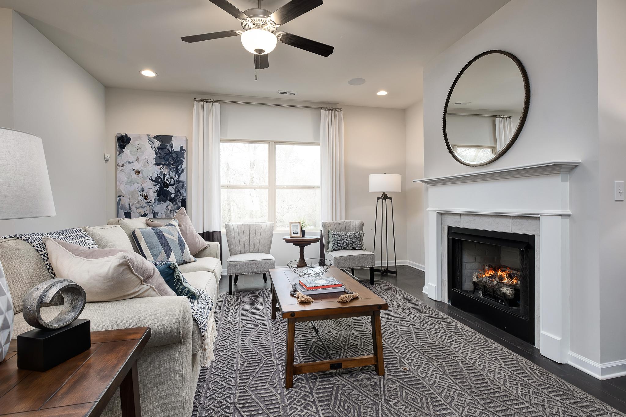 Cozy living room with white fireplace, plush sofa, patterned rug, and ceiling fan at The Reserve at Overton in Hampton Cove, Alabama