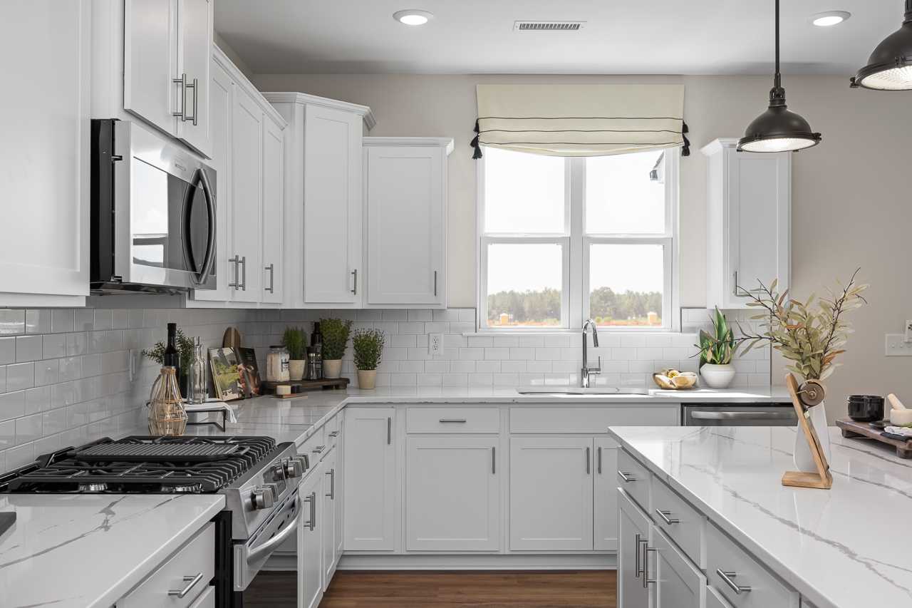 Spacious white shaker kitchen in Wellers Knoll Lillington NC with quartz island, subway tile backsplash, stainless appliances and pendant lights