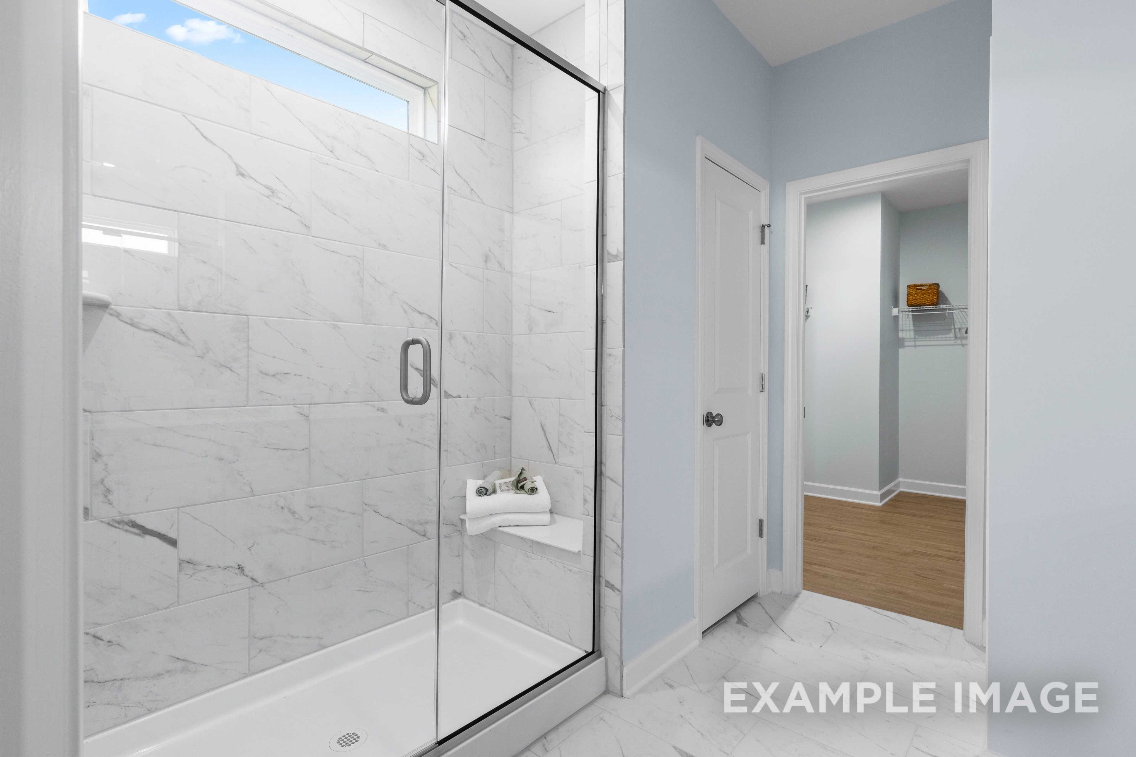Spacious master bathroom in The Ash C with frameless glass shower, white marble tiles, and towel niche