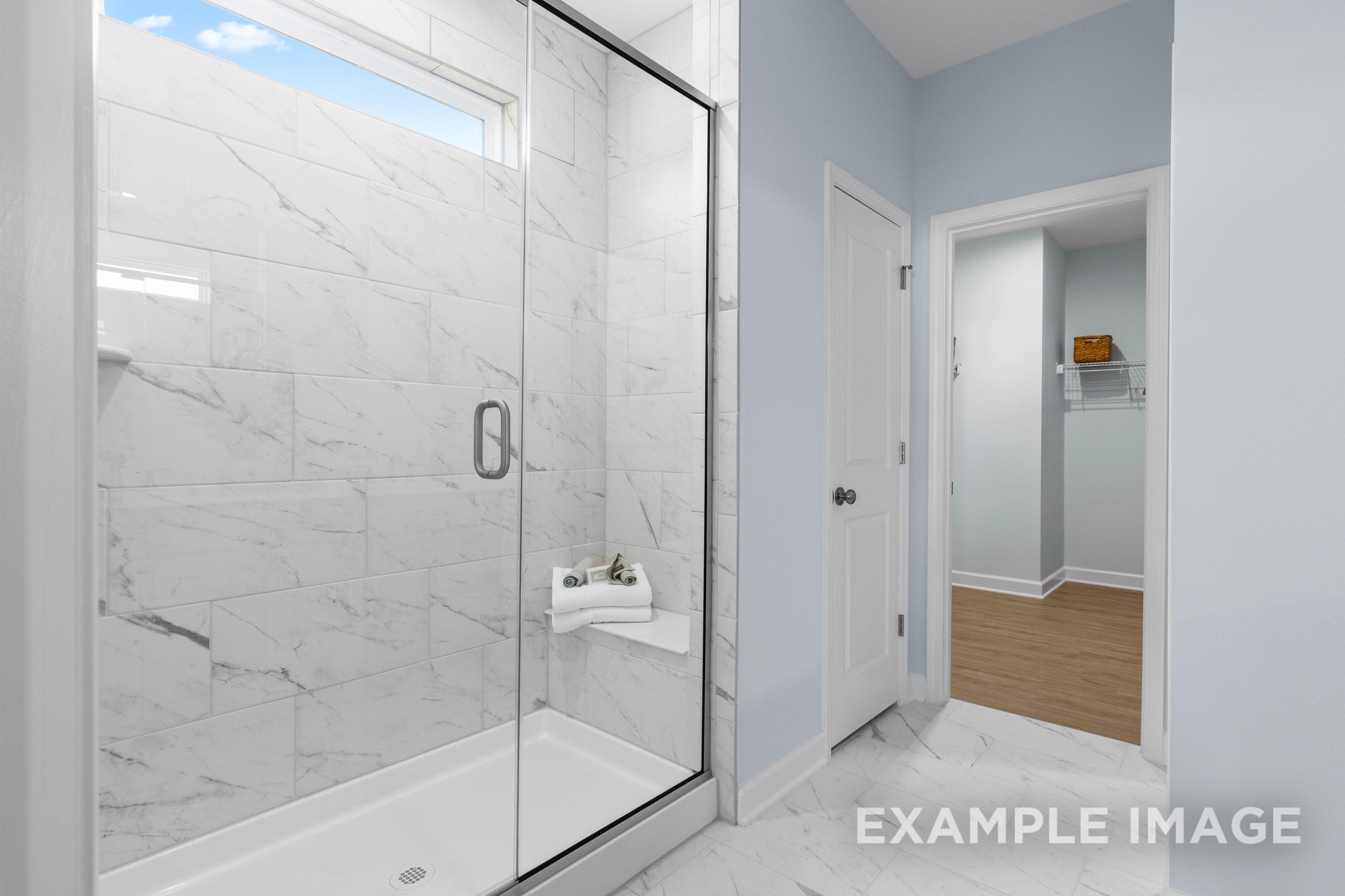 Spacious master bathroom in The Ash C with frameless glass shower, white marble tiles, and towel niche
