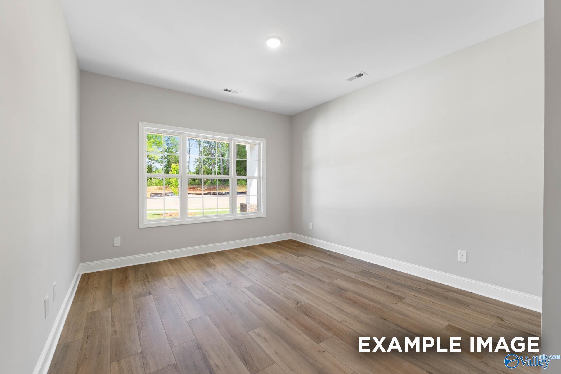 Bright empty bedroom with wood-look flooring and large window in Davidson Homes Chelsea B plan, The Meadows, Athens, Alabama