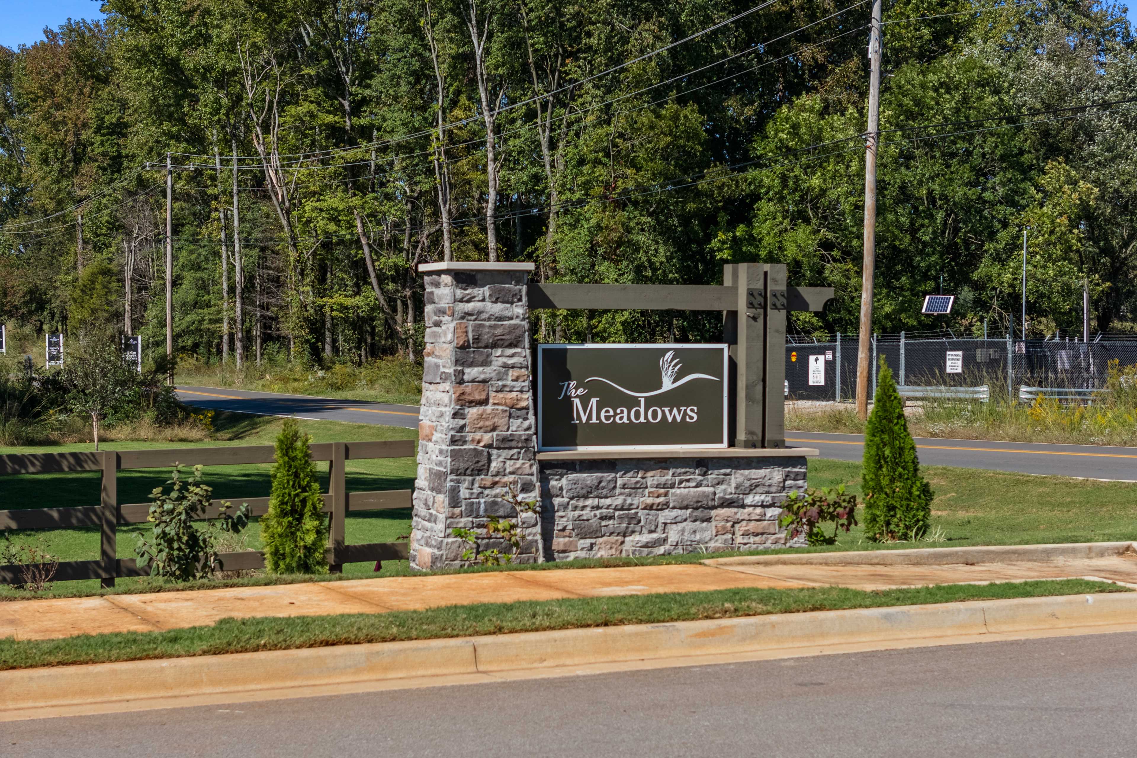 The Meadows entrance sign in Athens Alabama with stone pillars, wooden signage, and surrounding trees