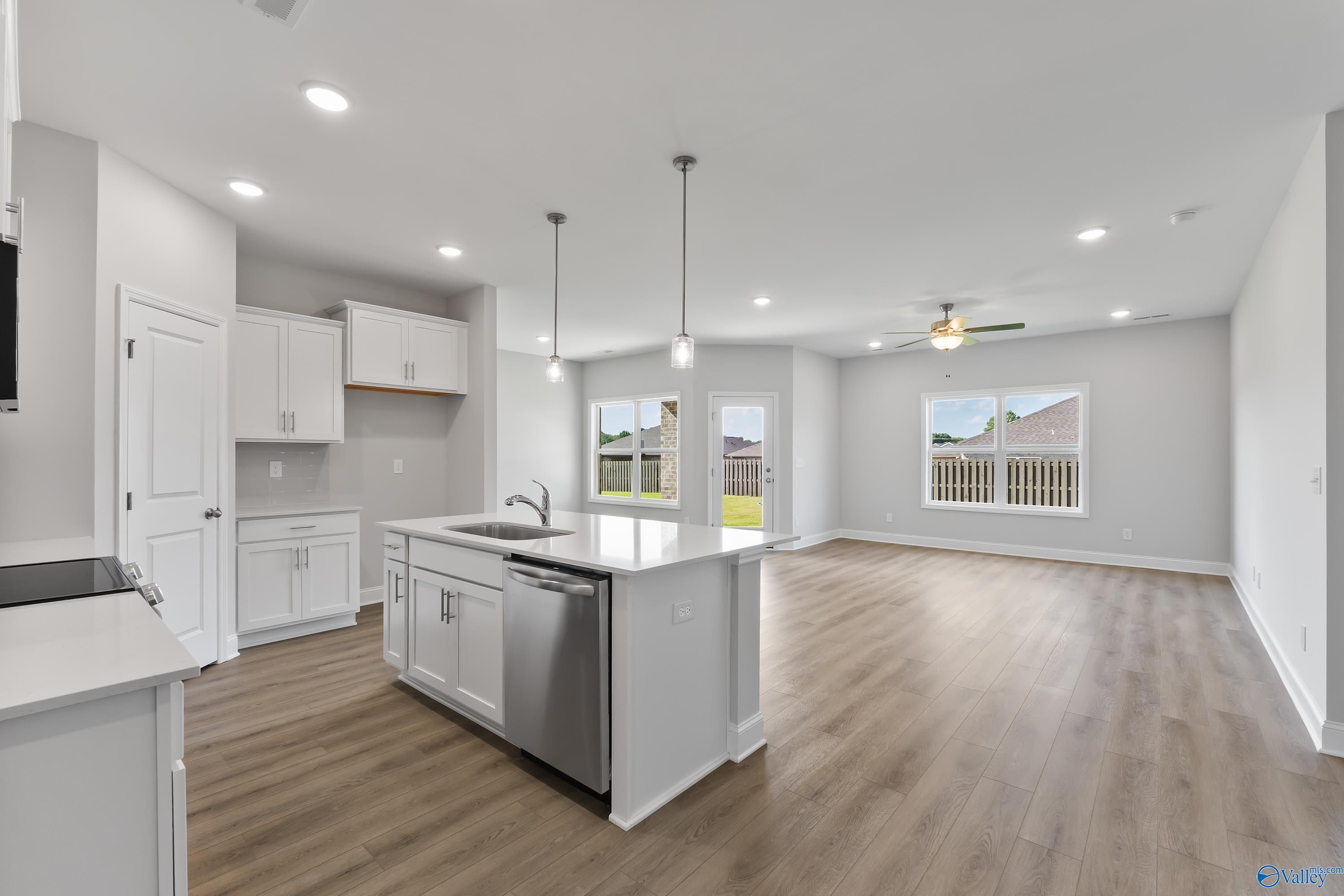 Modern open-concept kitchen with white shaker cabinets, large island sink, and backyard view in Davidson Homes The Daphne, Hazel Green, AL
