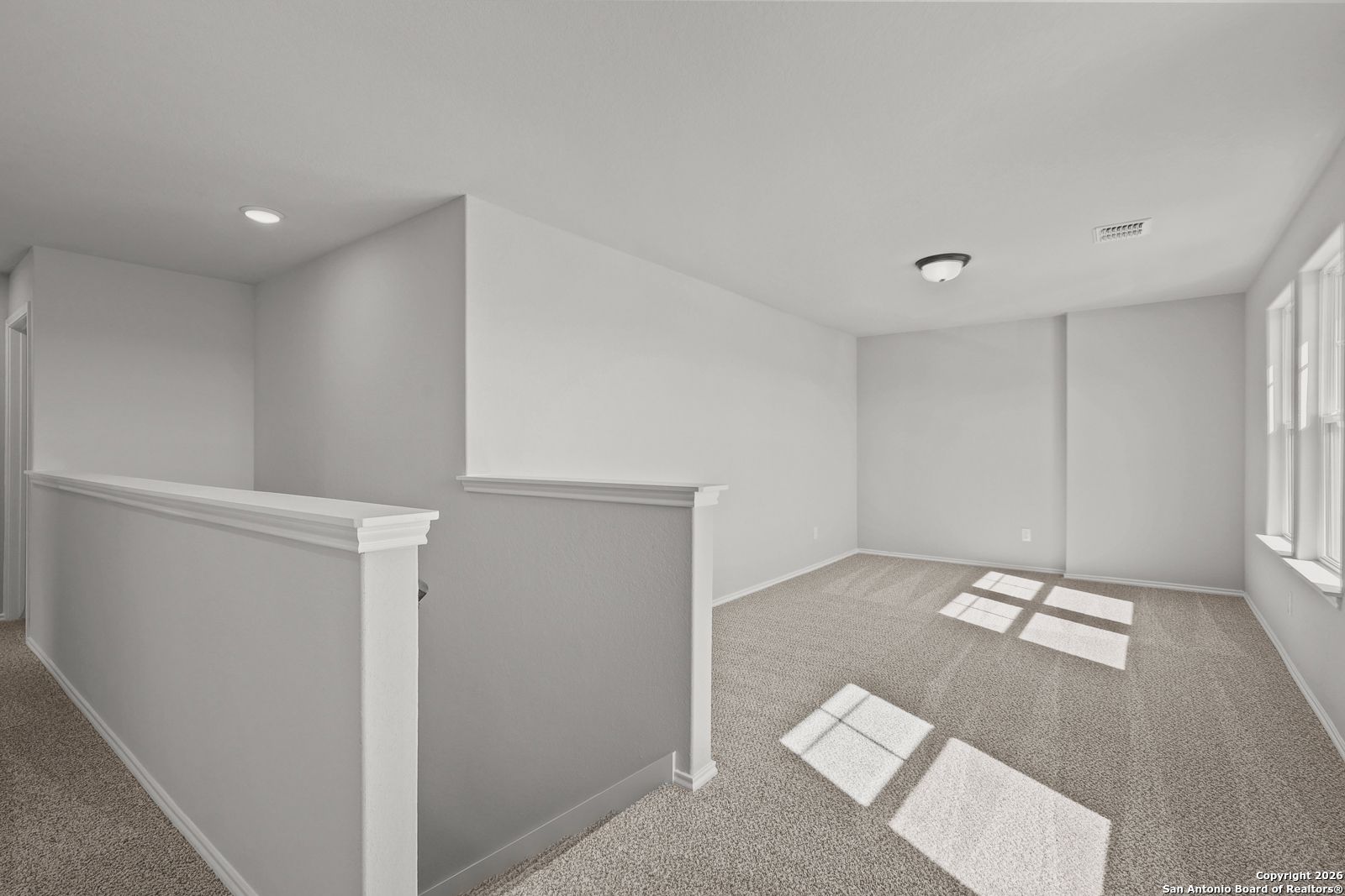 Bright upstairs loft with beige carpet, large sunny windows, and open railing in Davidson Homes The Murray K, San Antonio