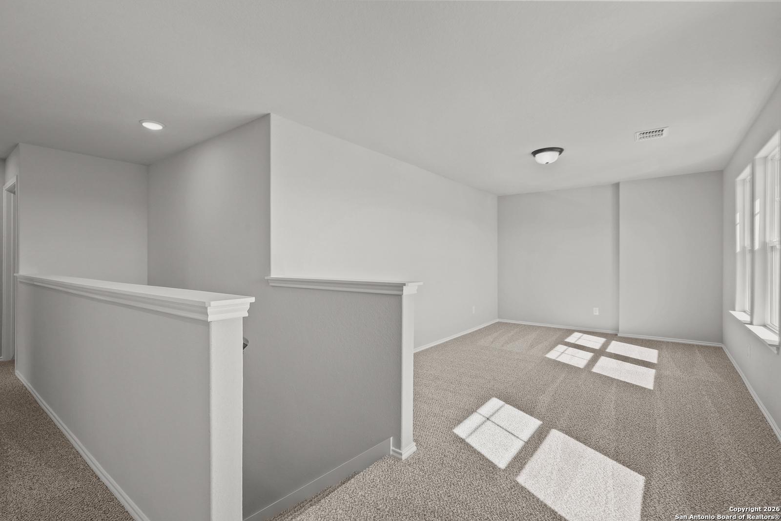 Bright upstairs loft with beige carpet, large sunny windows, and open railing in Davidson Homes The Murray K, San Antonio