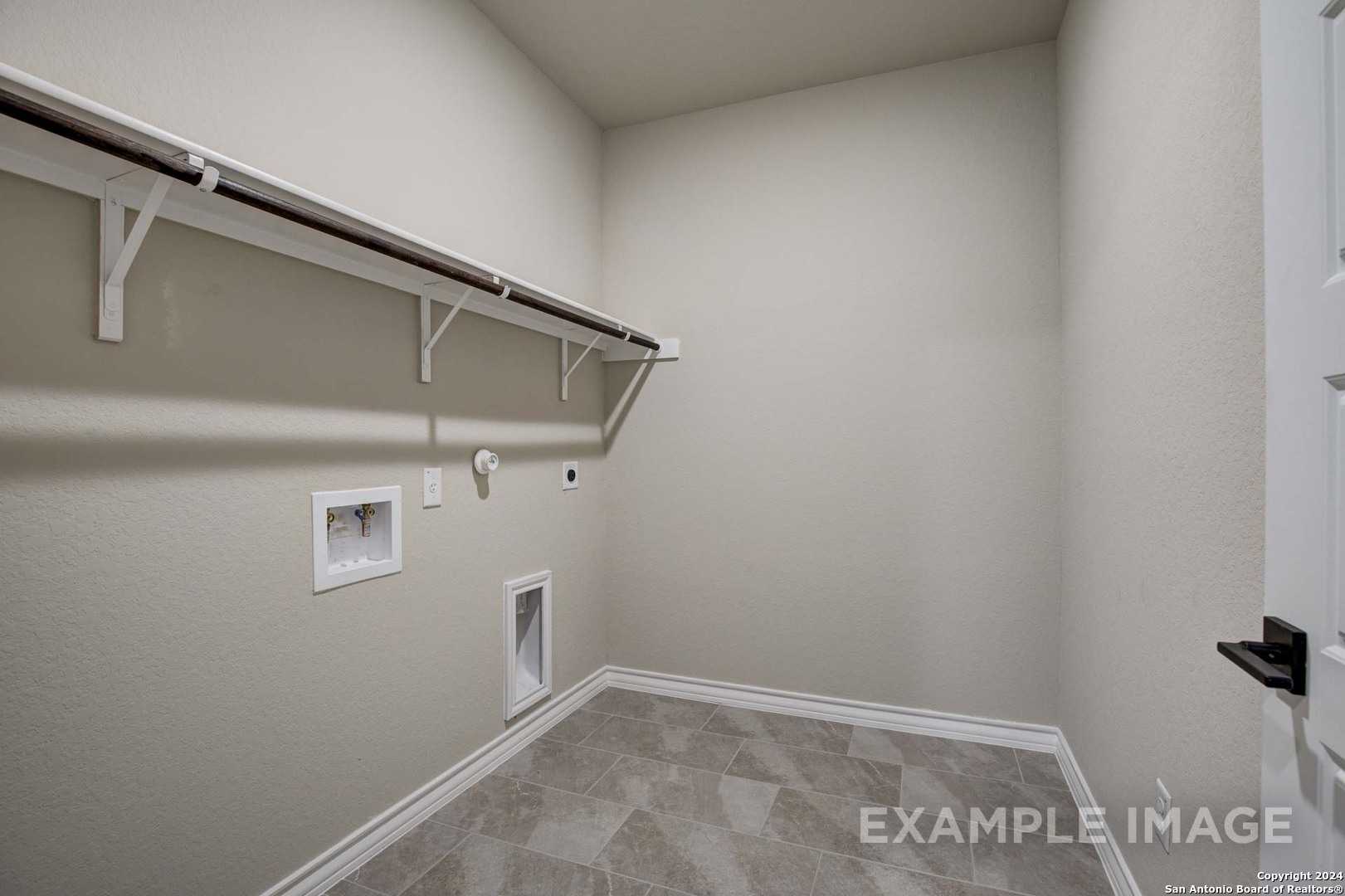 Spacious laundry room with wooden shelves, utility sink, washer hookups, and tiled floor in Davidson Homes The Rockford G, Ladera, San Antonio