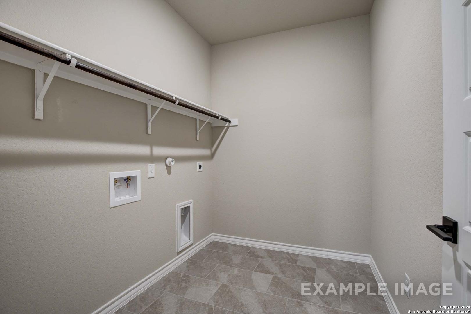 Spacious laundry room with wooden shelves, utility sink, washer hookups, and tiled floor in Davidson Homes The Rockford G, Ladera, San Antonio