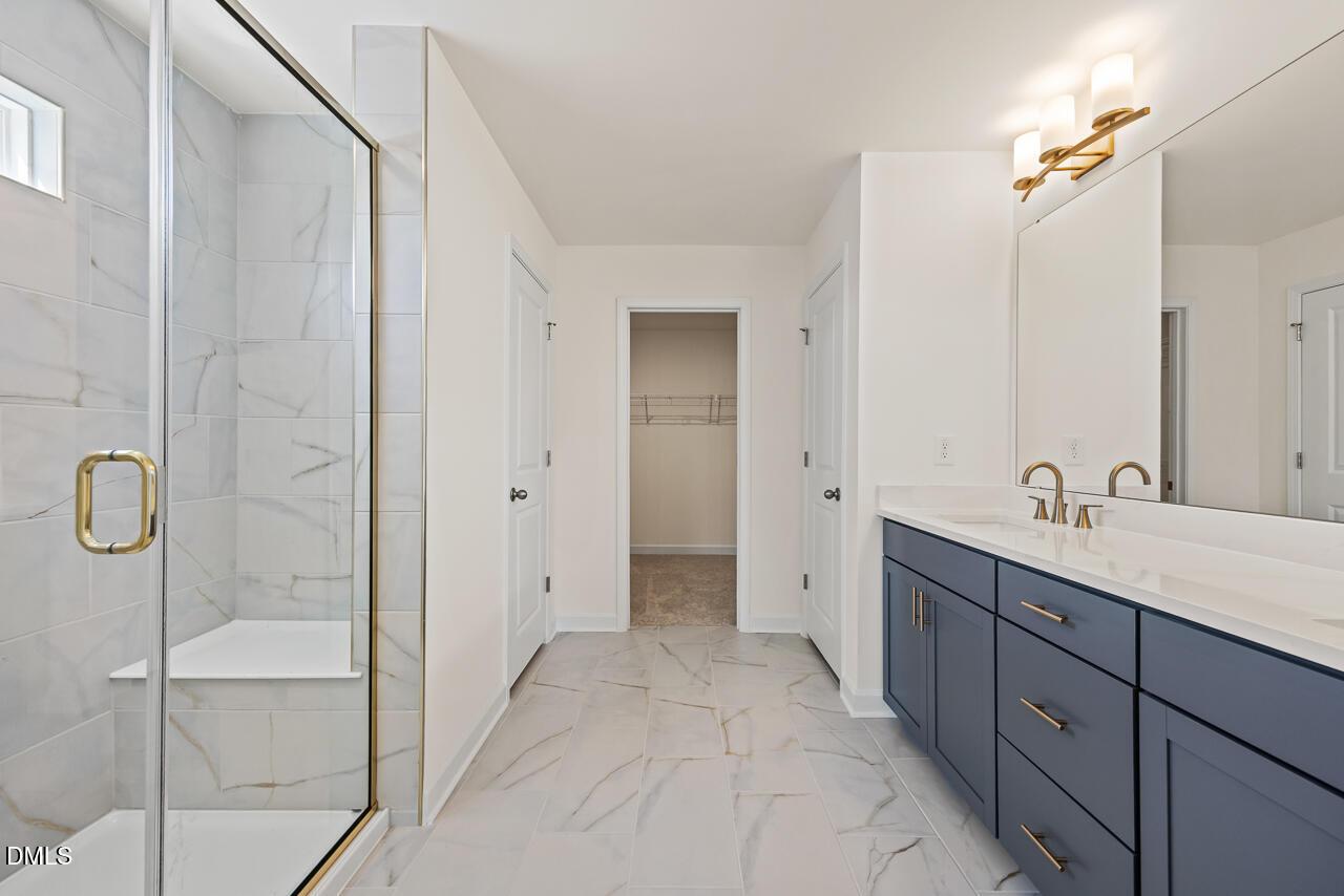 Elegant primary bathroom with glass walk-in shower, navy double vanity, and gold fixtures in Davidson Homes Hickory II B, Lillington NC