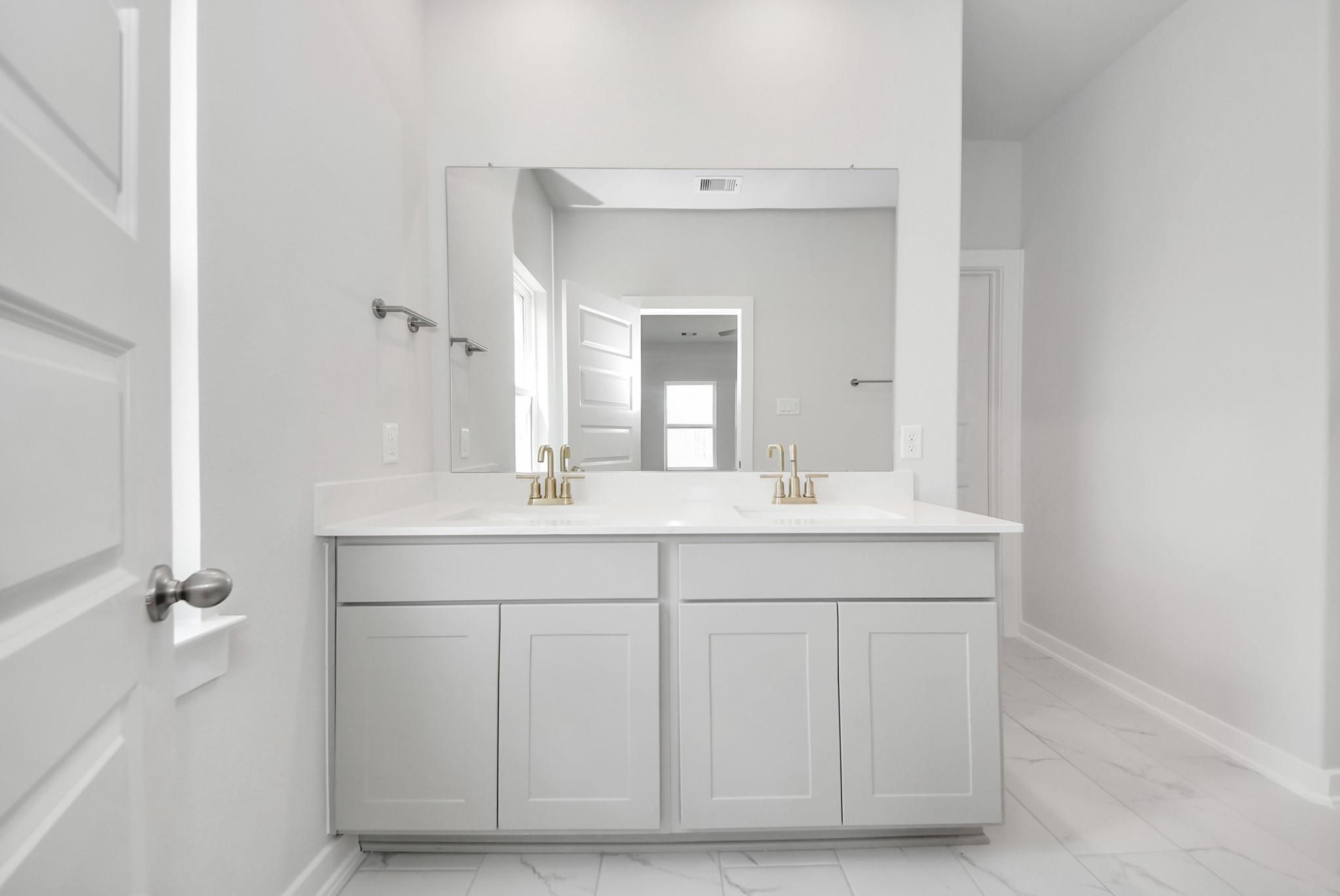 Modern double vanity with gold faucets and white countertops in Davidson Homes The Verano B floor plan in Sunterra, Katy.