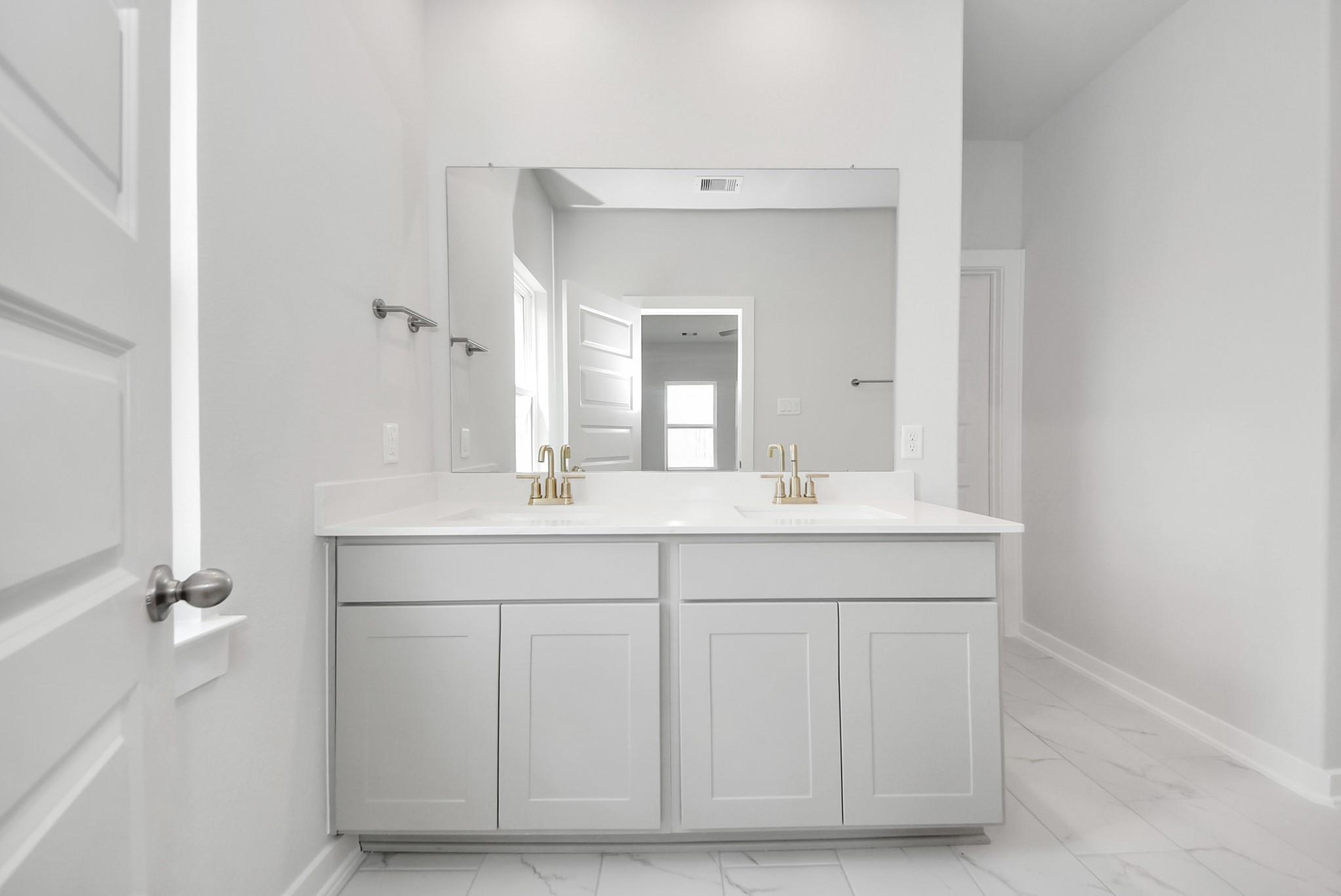 Modern double vanity with gold faucets and white countertops in Davidson Homes The Verano B floor plan in Sunterra, Katy.