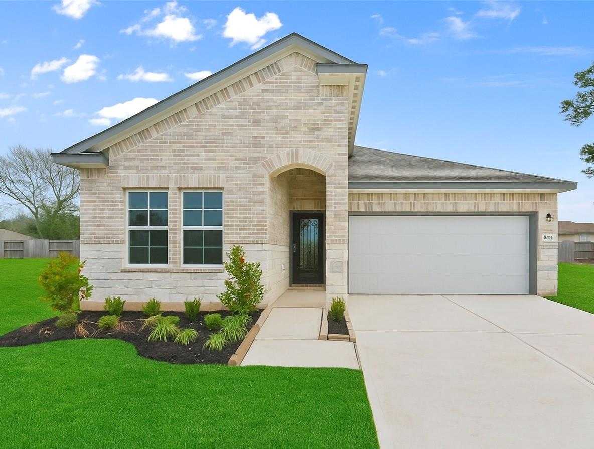 Modern beige brick single-story home with arched entry, large windows, 2-car garage, and landscaped yard in Windmill Estates, Magnolia, Texas